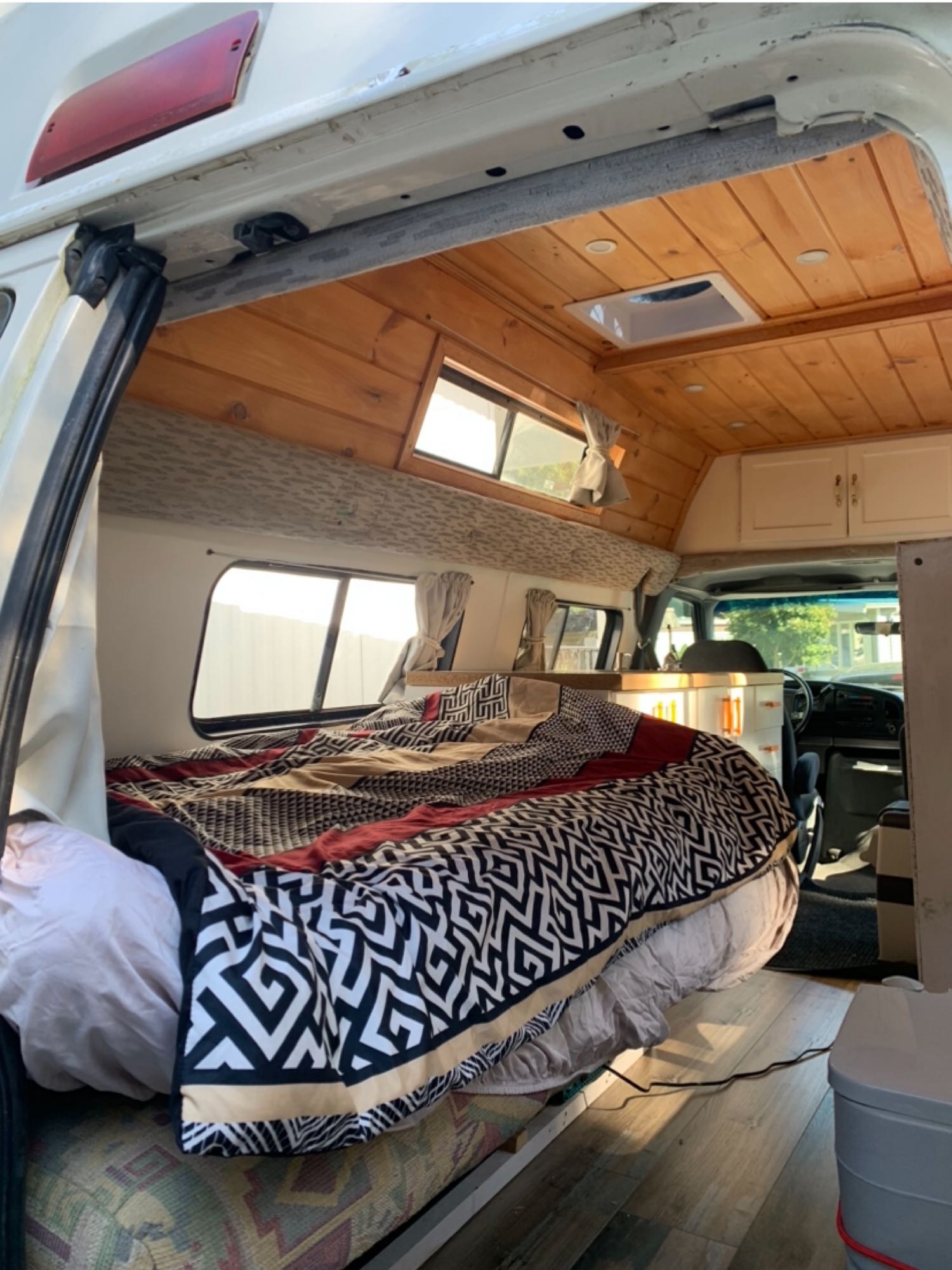Explore in comfort! This RV rental features a cozy bed with patterned bedding, wood ceiling, and bright windows.. Ford Econoline Club Wagon 1994