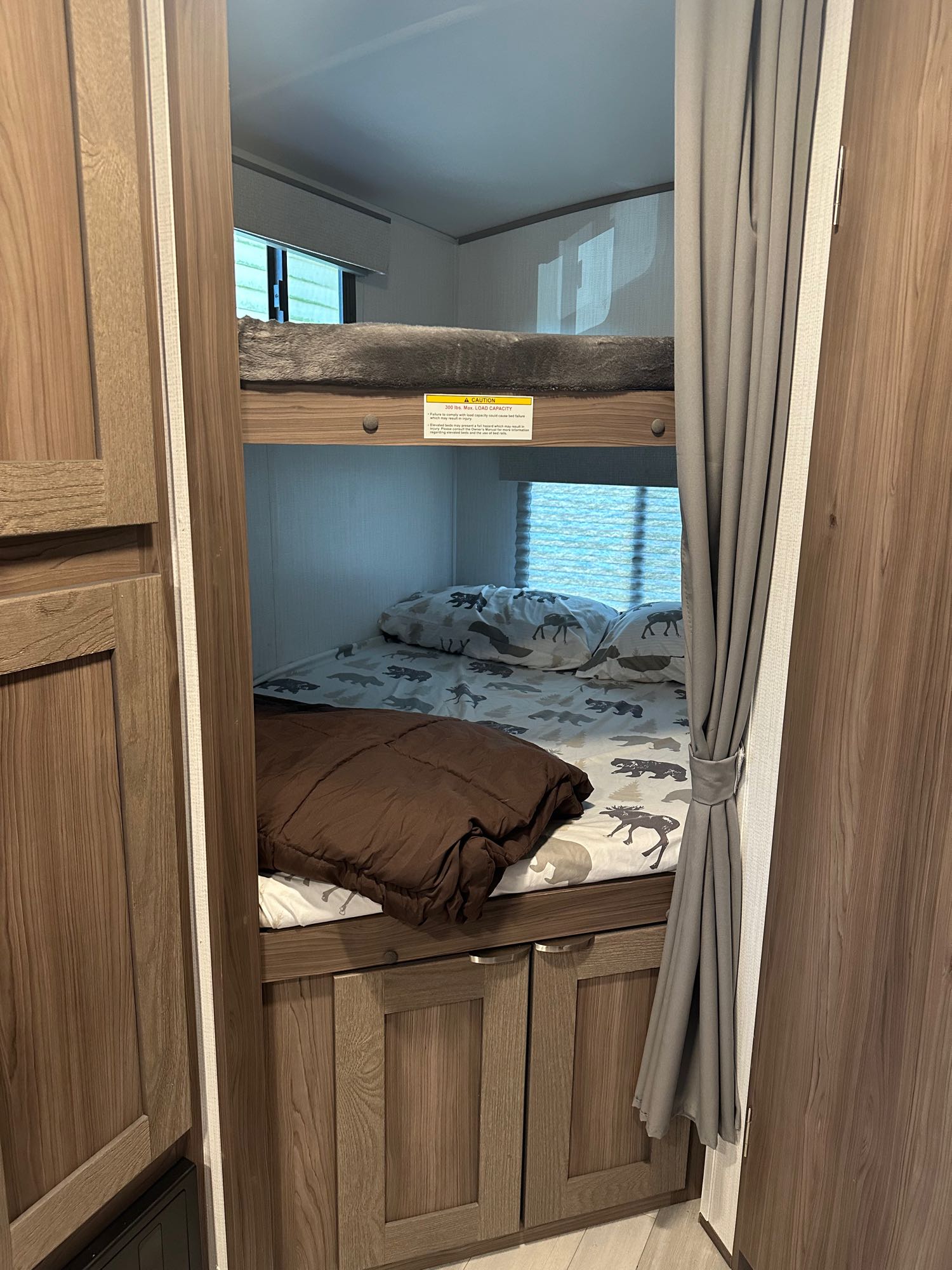 An RV rental's cozy bunk beds, with patterned bedding and a brown comforter, feature a visible 300 lbs. max load capacity sign.. Cruiser RV MPG 2500bh 2024