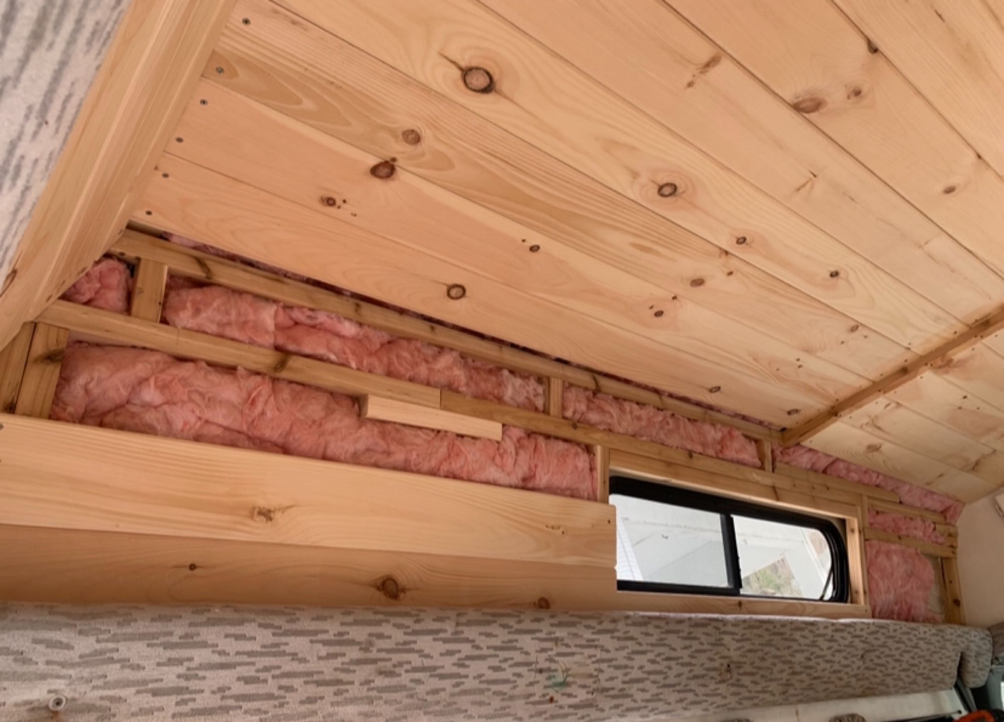 RV rental renovation showing new wood ceiling, visible pink insulation & wood framing by a window.. Ford Econoline Club Wagon 1994