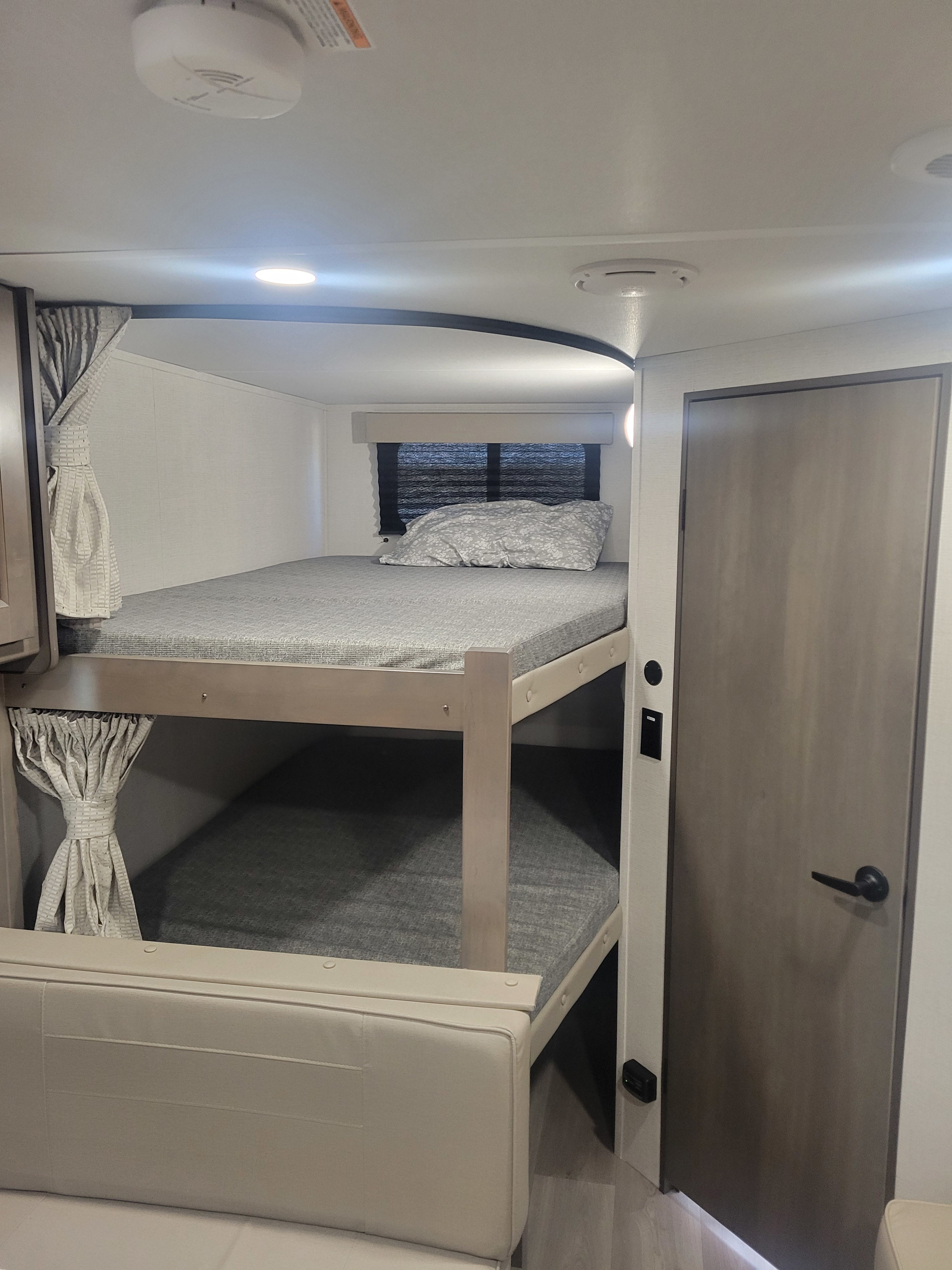 Interior of an RV rental, showcasing cozy bunk beds with grey mattresses. The upper bunk features a small window, ideal for family travel.. Transcend 247bhx 2024