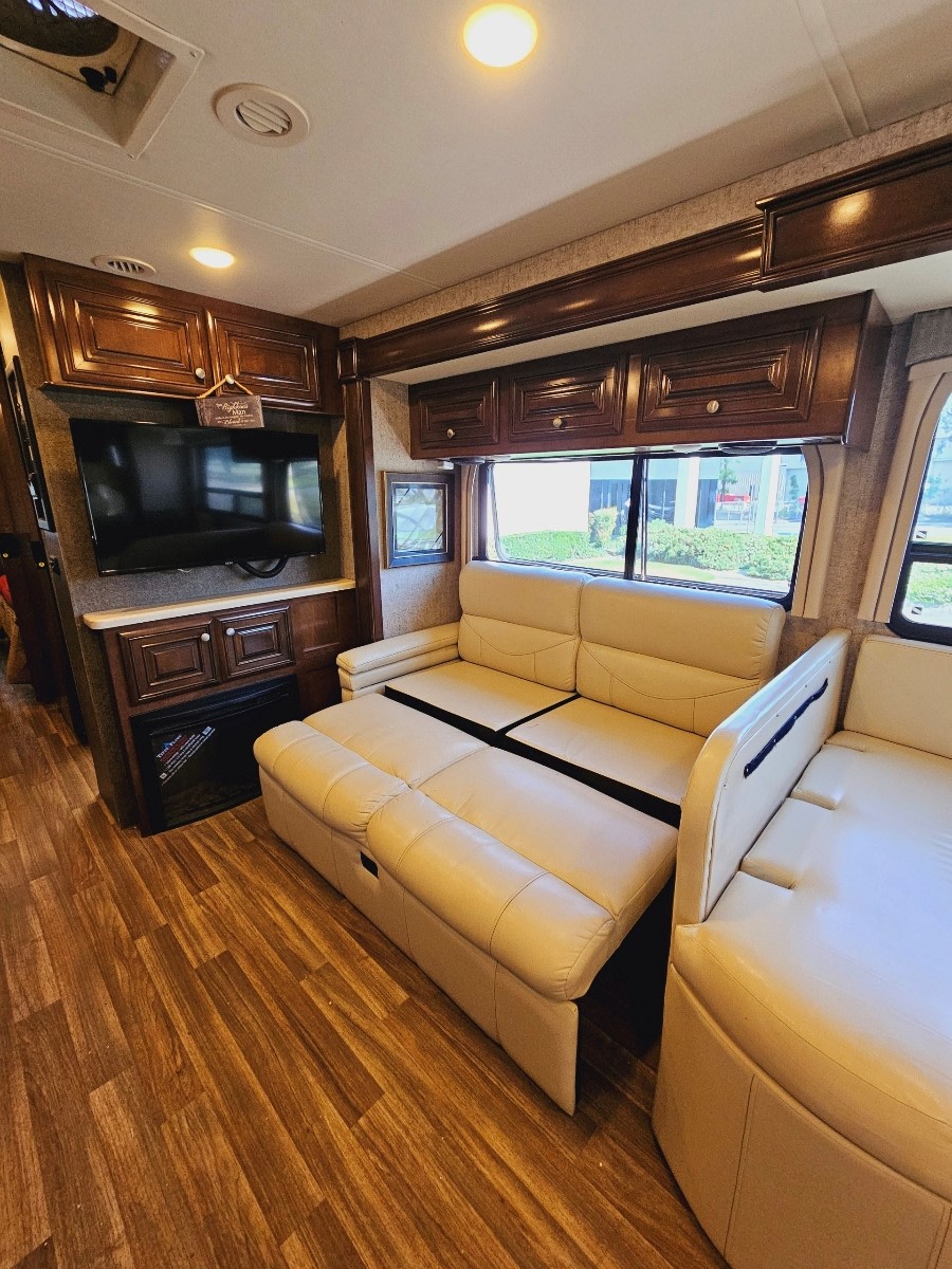Spacious RV rental living area: light-colored sofa bed partially extended, TV, and wood cabinetry & floors.. Thor Miramar 2017