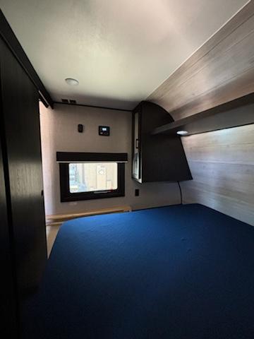 Well-lit RV rental bedroom showing a large blue bed, window, and dark wood cabinetry.. Jayco Jay Flight 2022