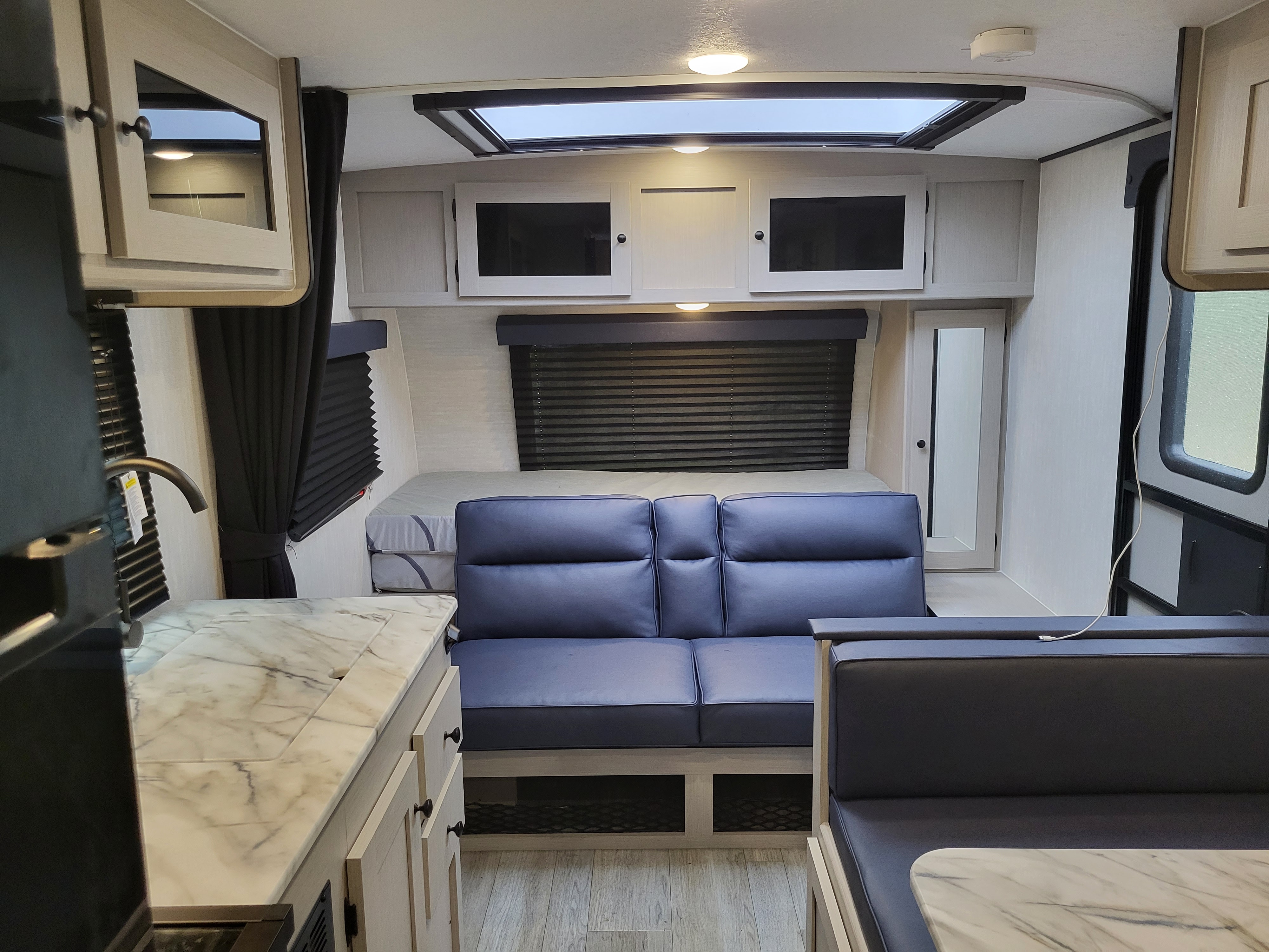 Inside a bright RV rental: view of the bed, comfortable blue sofa, kitchen counter, and dinette area.. Coachman Apex Nano 186BH 2025