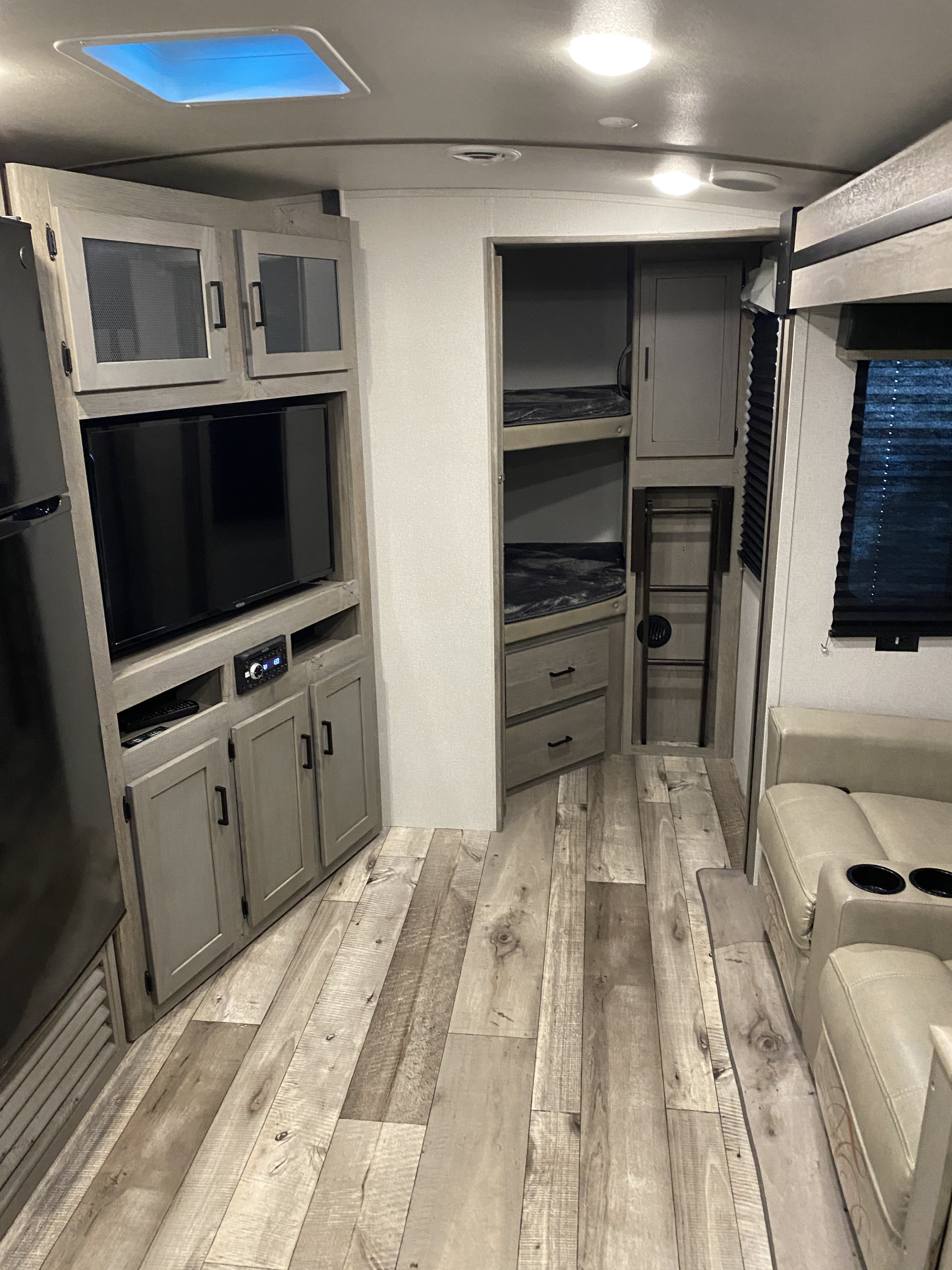 Spacious rv rental interior showing a living area with TV, built-in entertainment, refrigerator, and bunk beds on light wood-style flooring.. Keystone RV Outback Ultra-Lite 2021