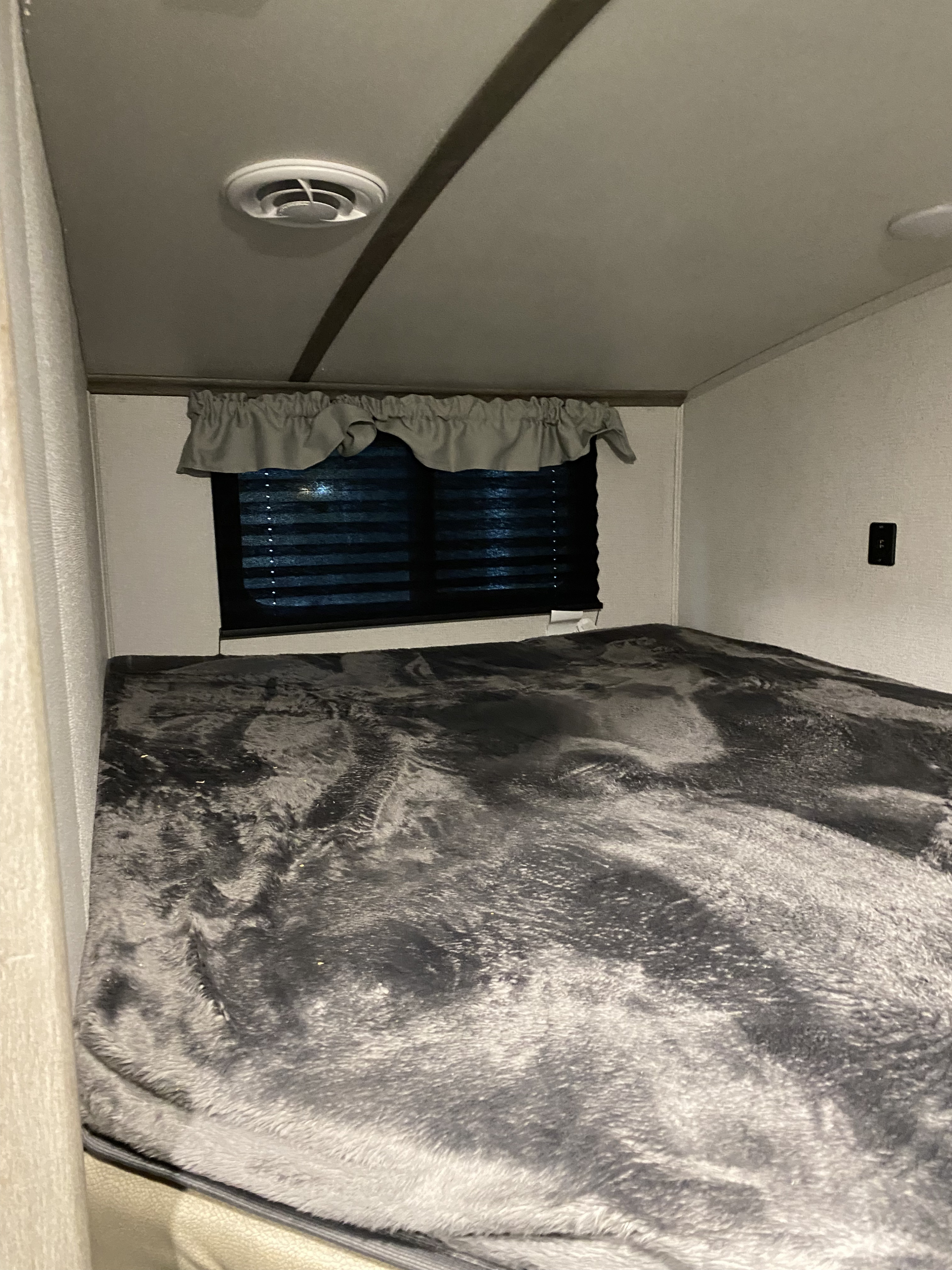 Cozy RV rental bunk bed interior with soft gray blanket, window, and ceiling vent. Perfect for a restful night.. Keystone RV Outback Ultra-Lite 2021