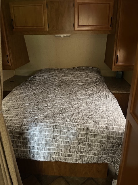 Cozy RV rental bedroom featuring a bed with a patterned comforter, overhead storage cabinets, and a reading light.. Outdoors RV Creekside 2013