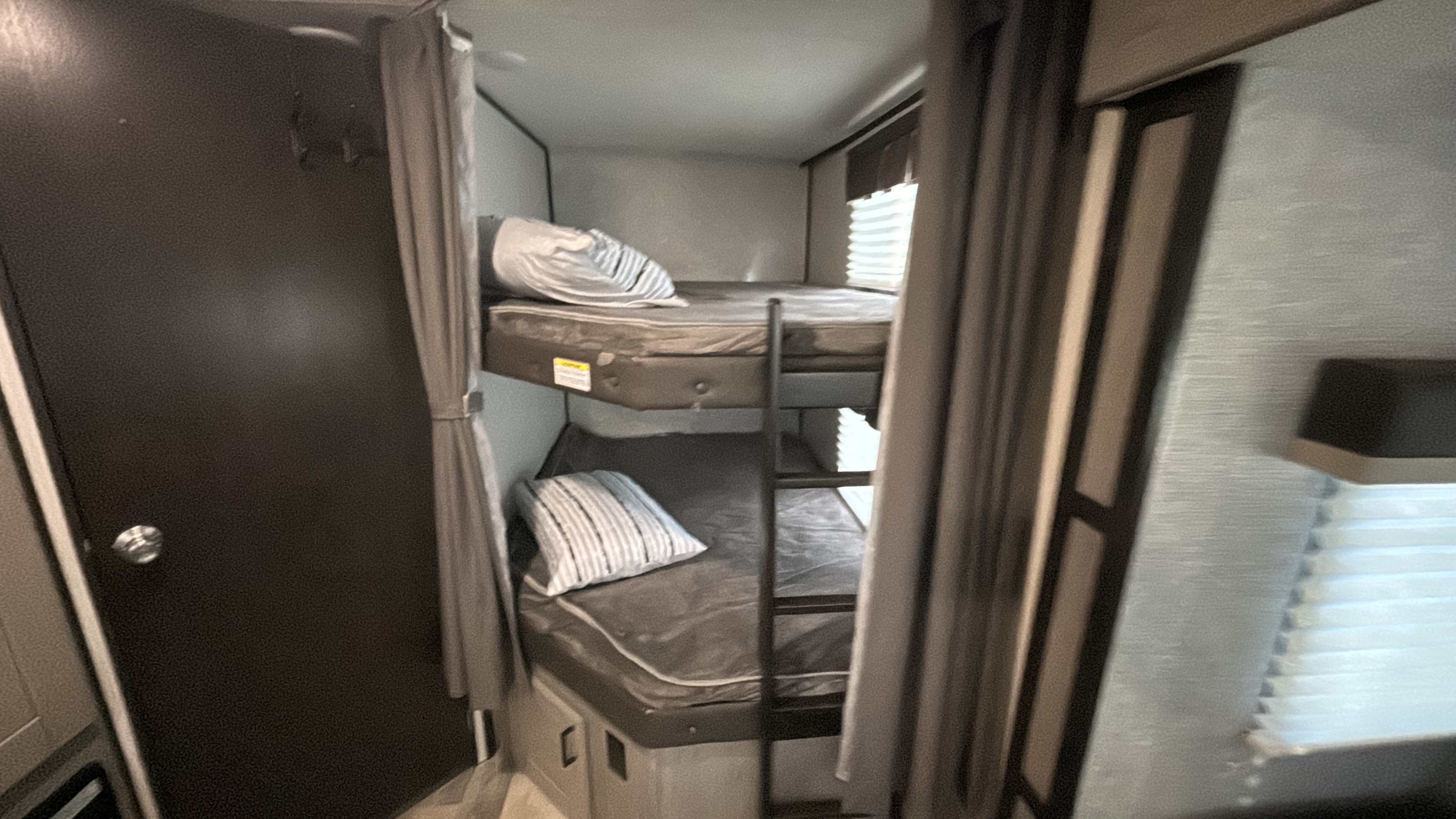Compact bunk beds inside an RV rental. Perfect sleeping area for family trips, with curtains for privacy and a nearby door.. Heartland m 2020