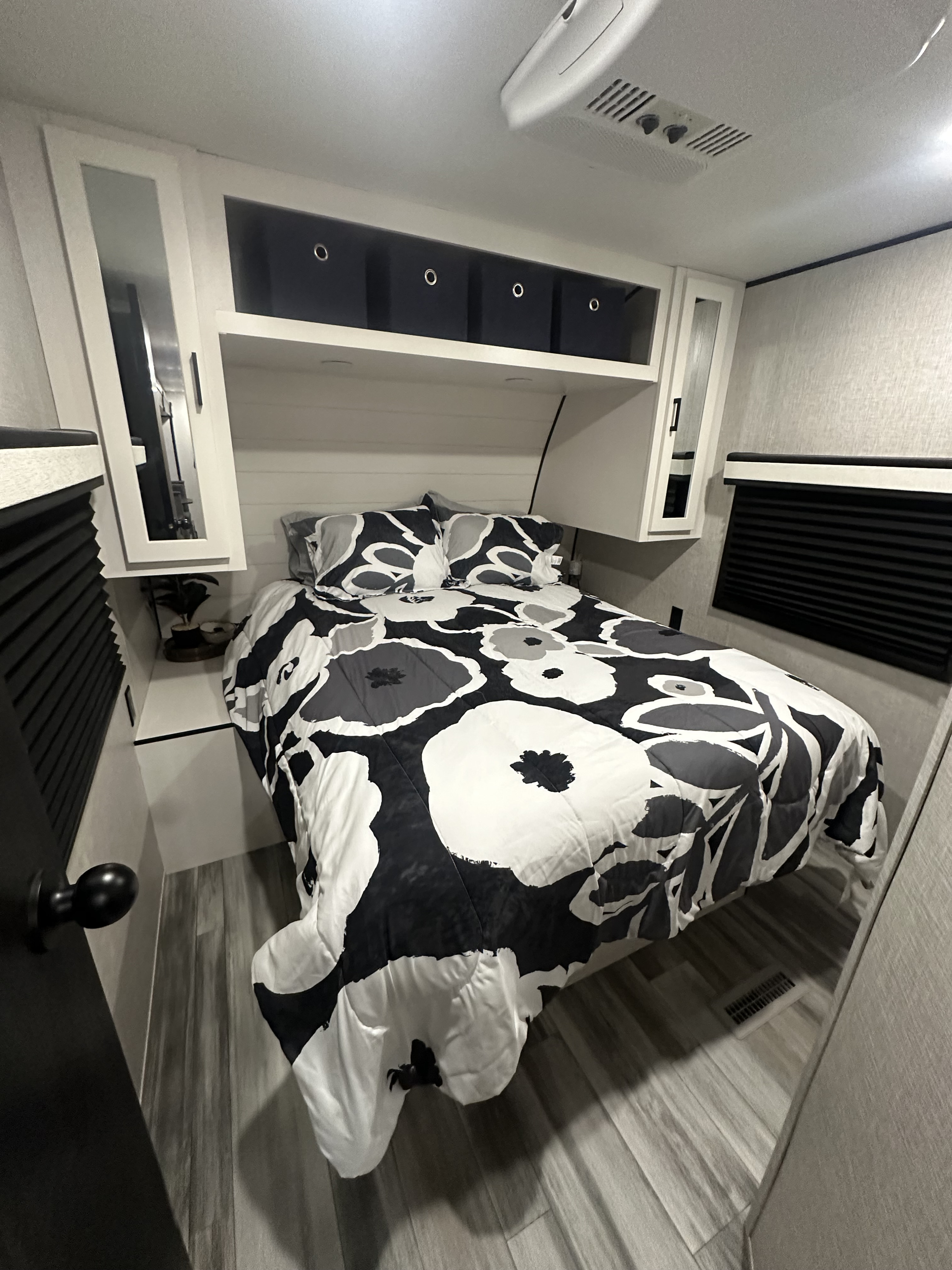 Comfortable RV rental bedroom featuring black, white, and gray floral bedding, overhead storage, and privacy blinds.. Jayco Jay Flight 2024