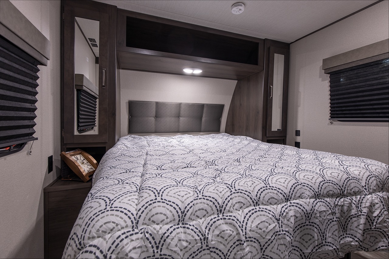 Cozy RV rental bedroom featuring a comfy bed, modern headboard, overhead cabinets, and compact storage.. Grand Design Transcend Xplor 221RB 2023