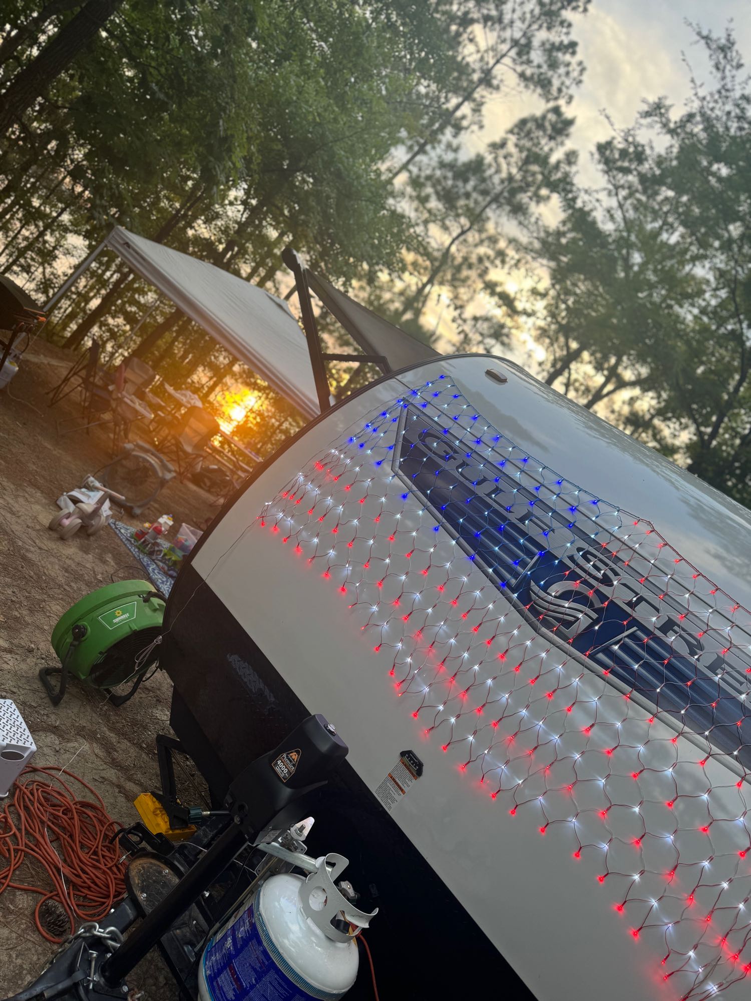 Enjoy a festive RV rental camping experience! This travel trailer with patriotic lights gleams at sunset in a wooded site.. Gulf Stream Kingsport 2023