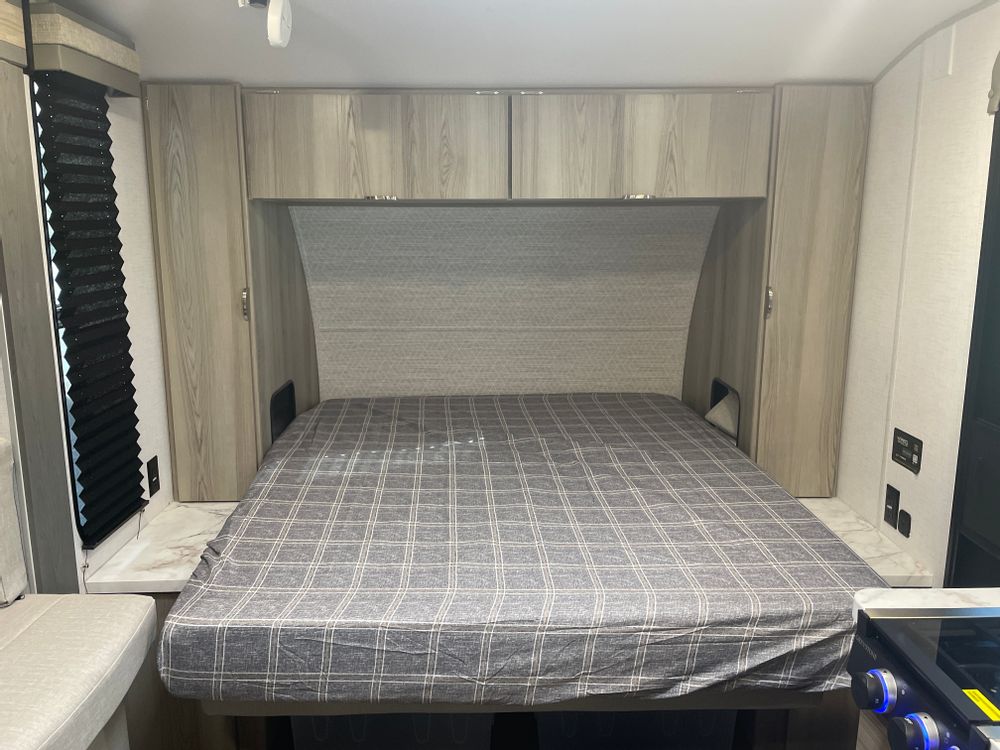 Inside an RV rental: a cozy bedroom features a bed with plaid cover, overhead cabinets, and side wardrobes.. Forest River Wildwood 2024