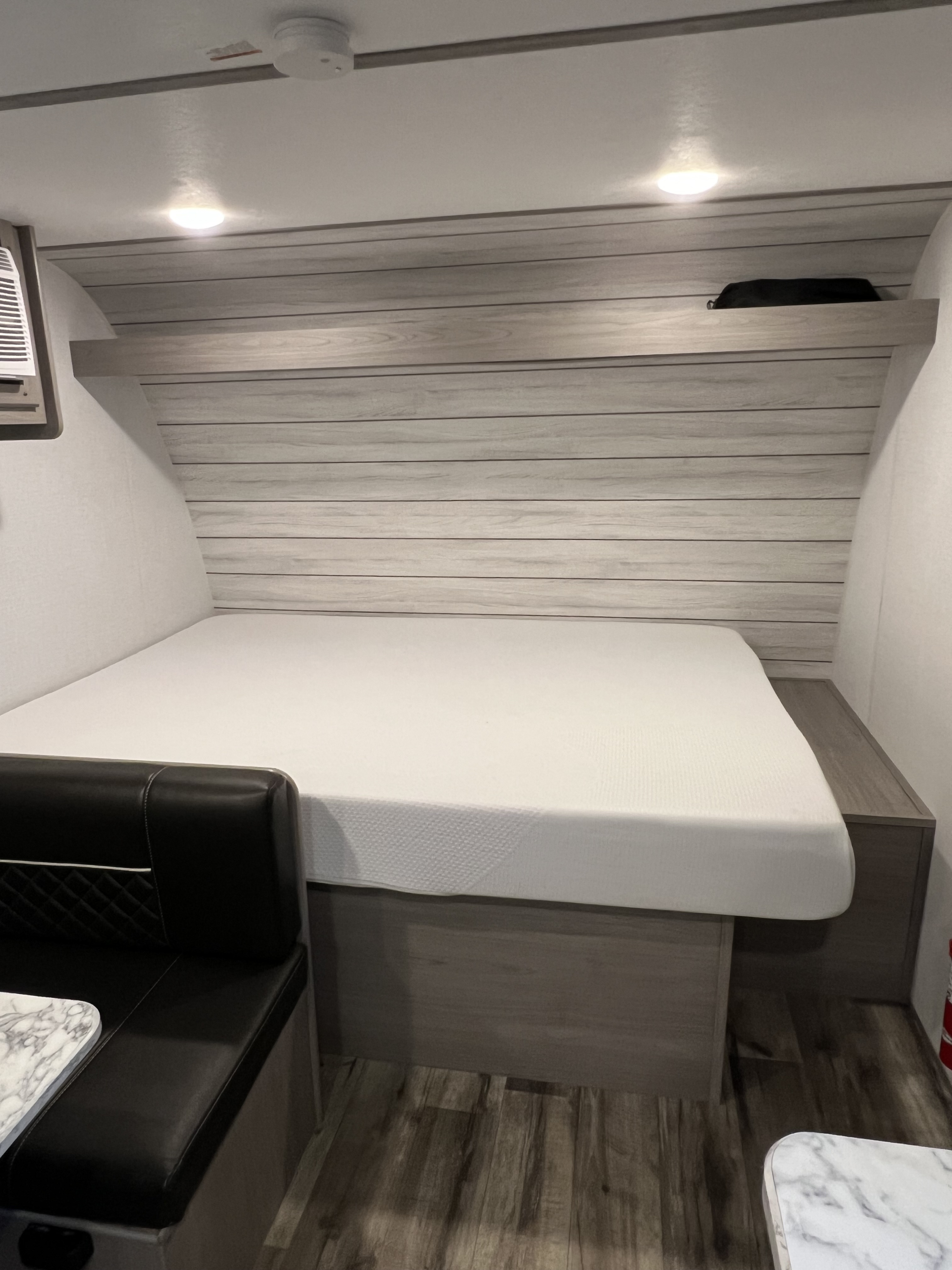 View inside an RV rental: white bed, black dinette with marble table, wood-paneled walls, and overhead storage.. Dutchmen Coleman Lantern LT 17B 2024