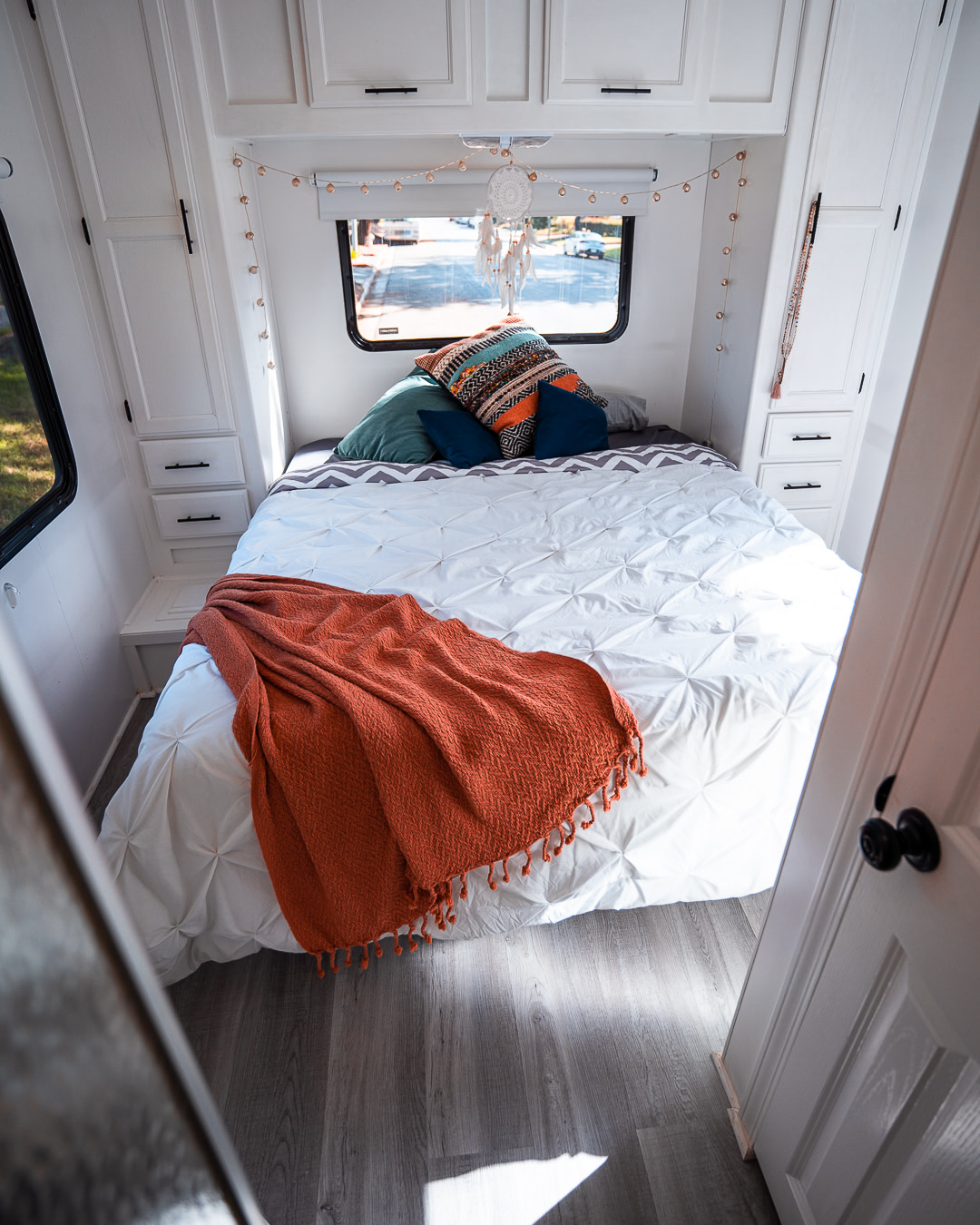 Cozy RV rental bedroom features a white interior, colorful pillows, an orange throw blanket, and a view of the street outside.. Gulf Stream Conquest Classic 2004