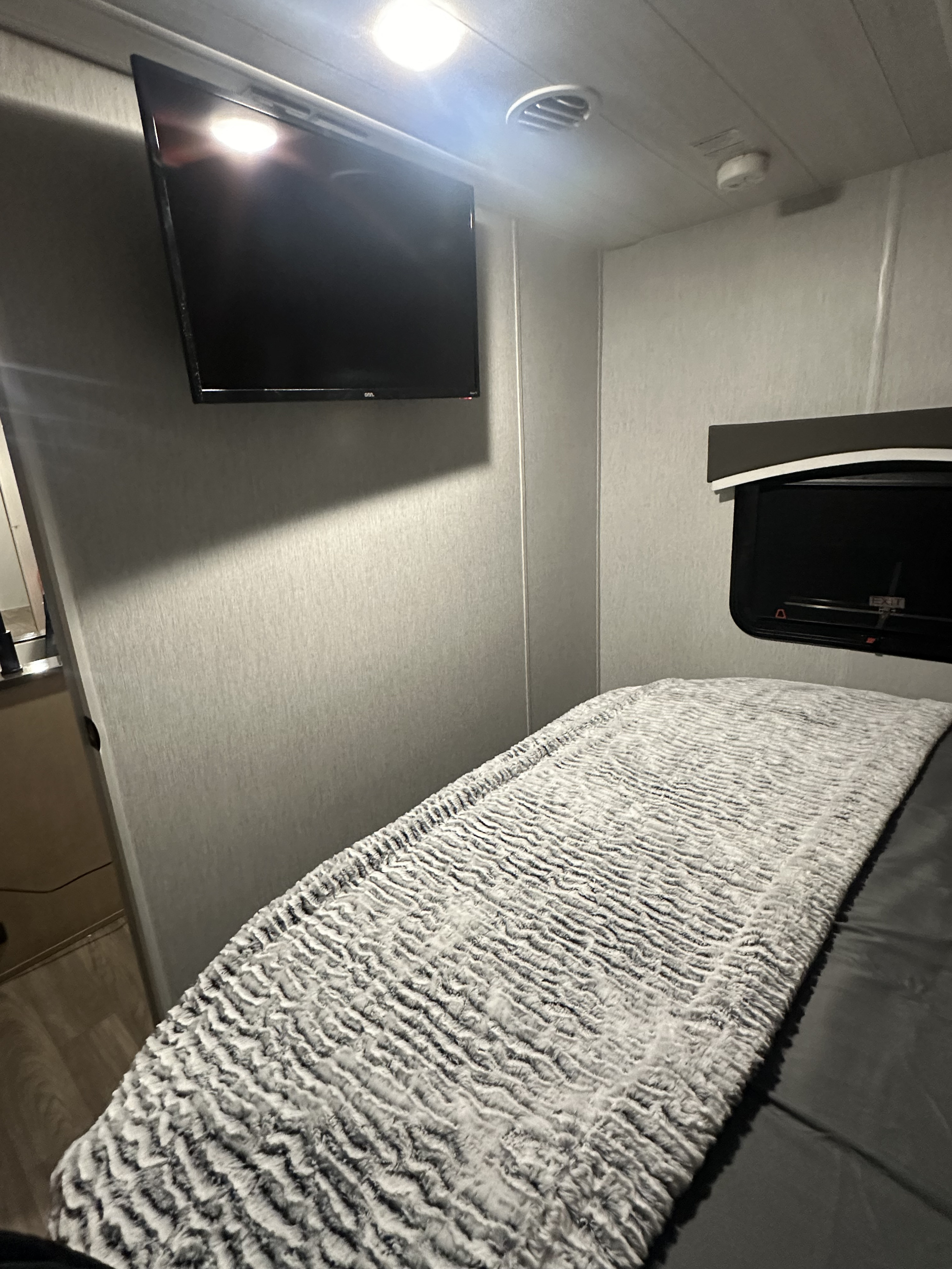 Inside an RV rental: a compact bedroom with mounted TV, comfy bed, and window. A cozy space.. Forest River Evo 2023