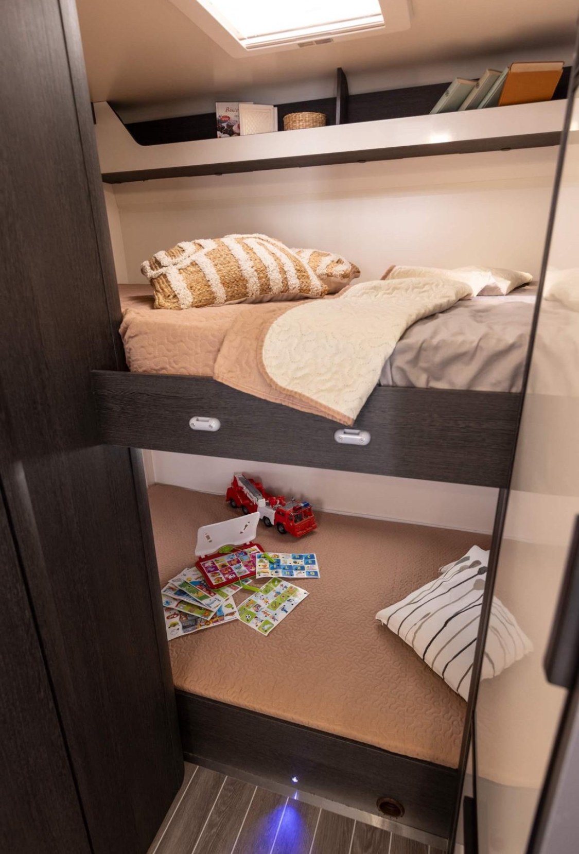 Cozy bunk beds in an RV rental, featuring a top bed with pillows and a bottom bed with kids' toys and a pillow.. Ford 675 Adventure 2024