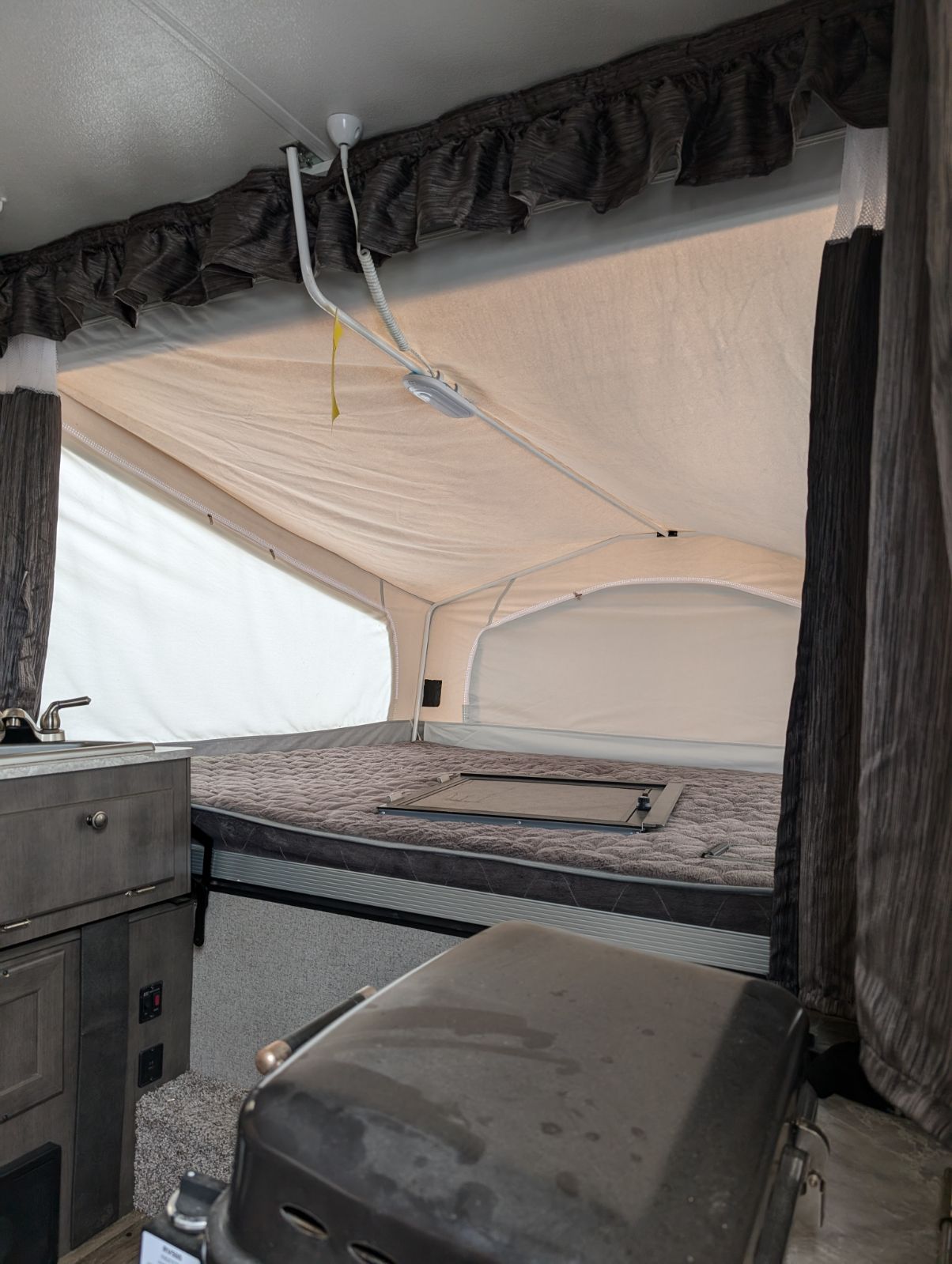 Explore this RV rental's pop-up camper interior, featuring a cozy bed, kitchen sink, and ample light for your next trip.. Rockwood 2318g 2019