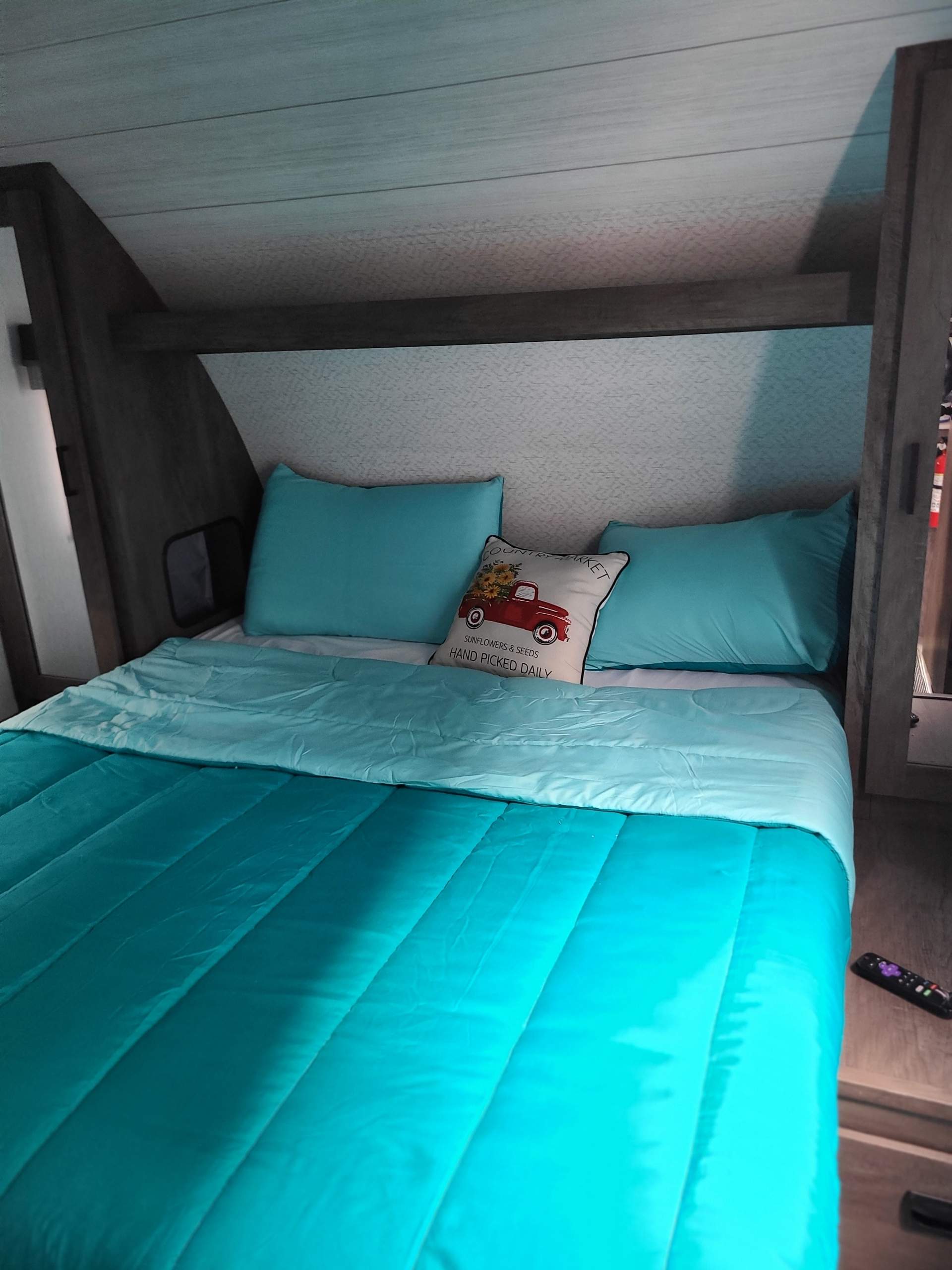 This cozy RV rental bedroom features a comfortable bed with vibrant teal bedding and a decorative sunflower pillow.. Forest River Wildwood X-Lite 2022