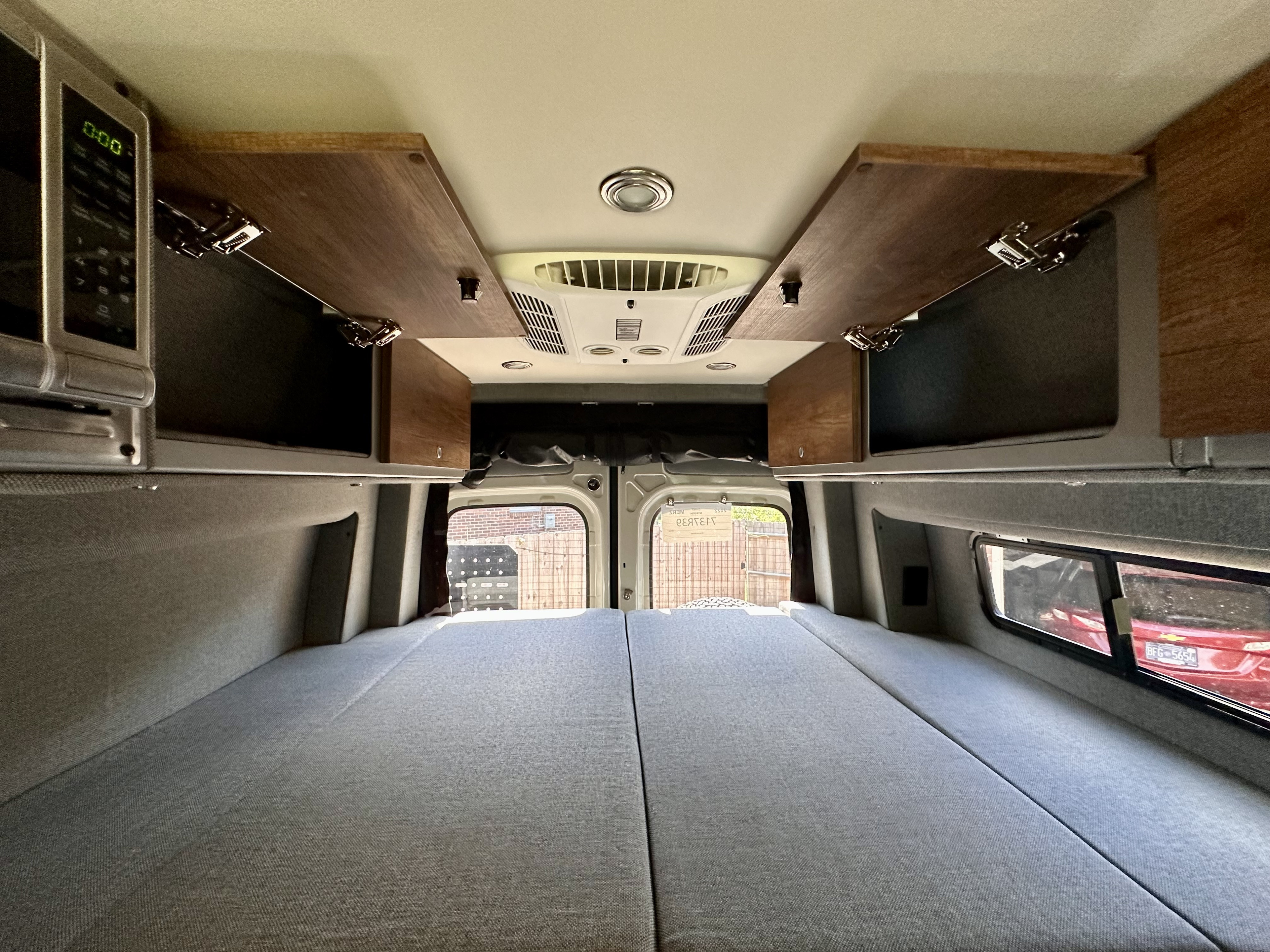 Inside an RV rental: a comfortable bed, overhead cabinets, microwave, and AC. Perfect for road trips.. Mercedes-Benz MB140 2022