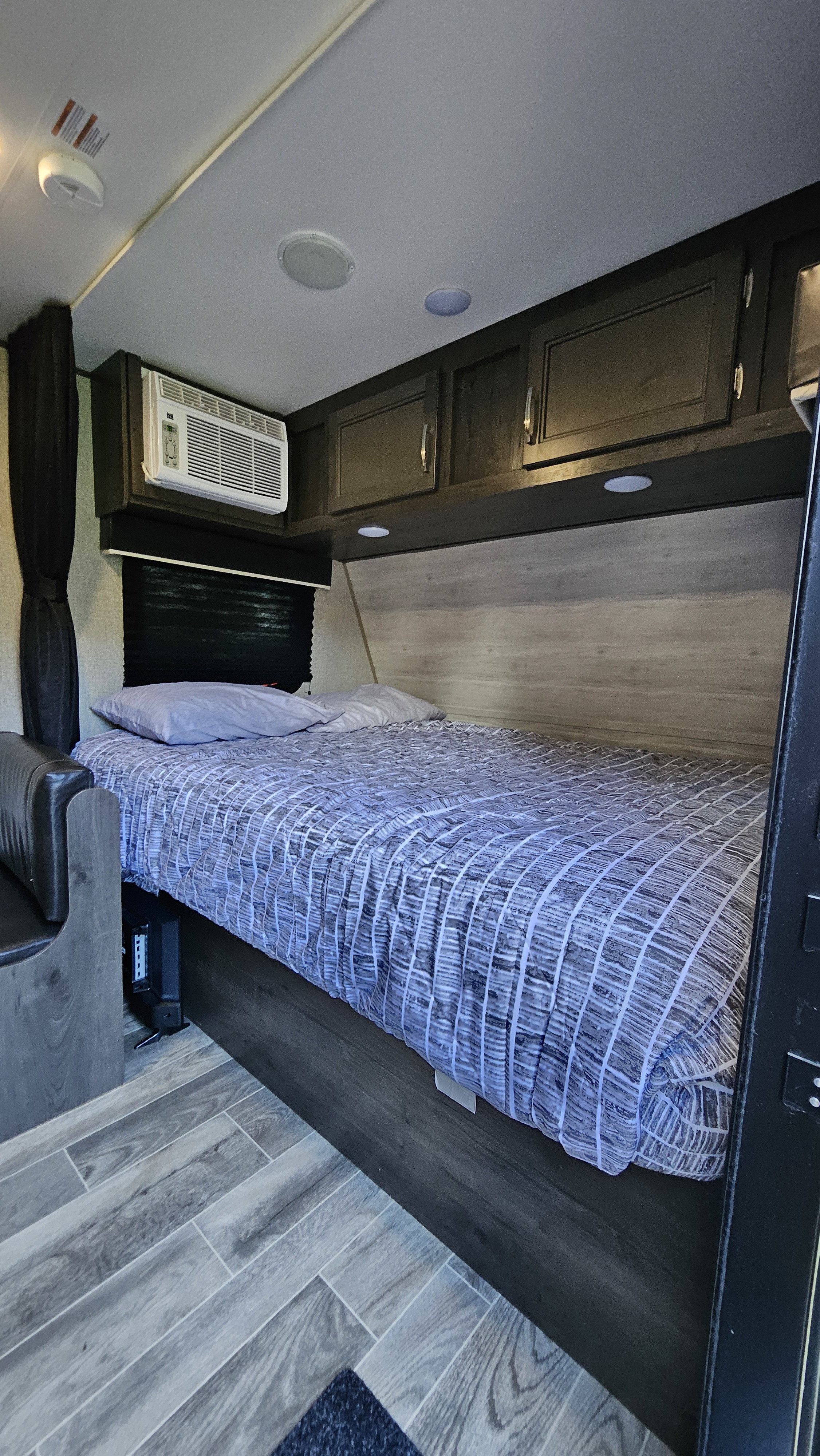 Cozy RV rental bedroom featuring a comfy bed, AC, overhead cabinets, and wood-look flooring.. Jayco Jay Flight SLX 2021