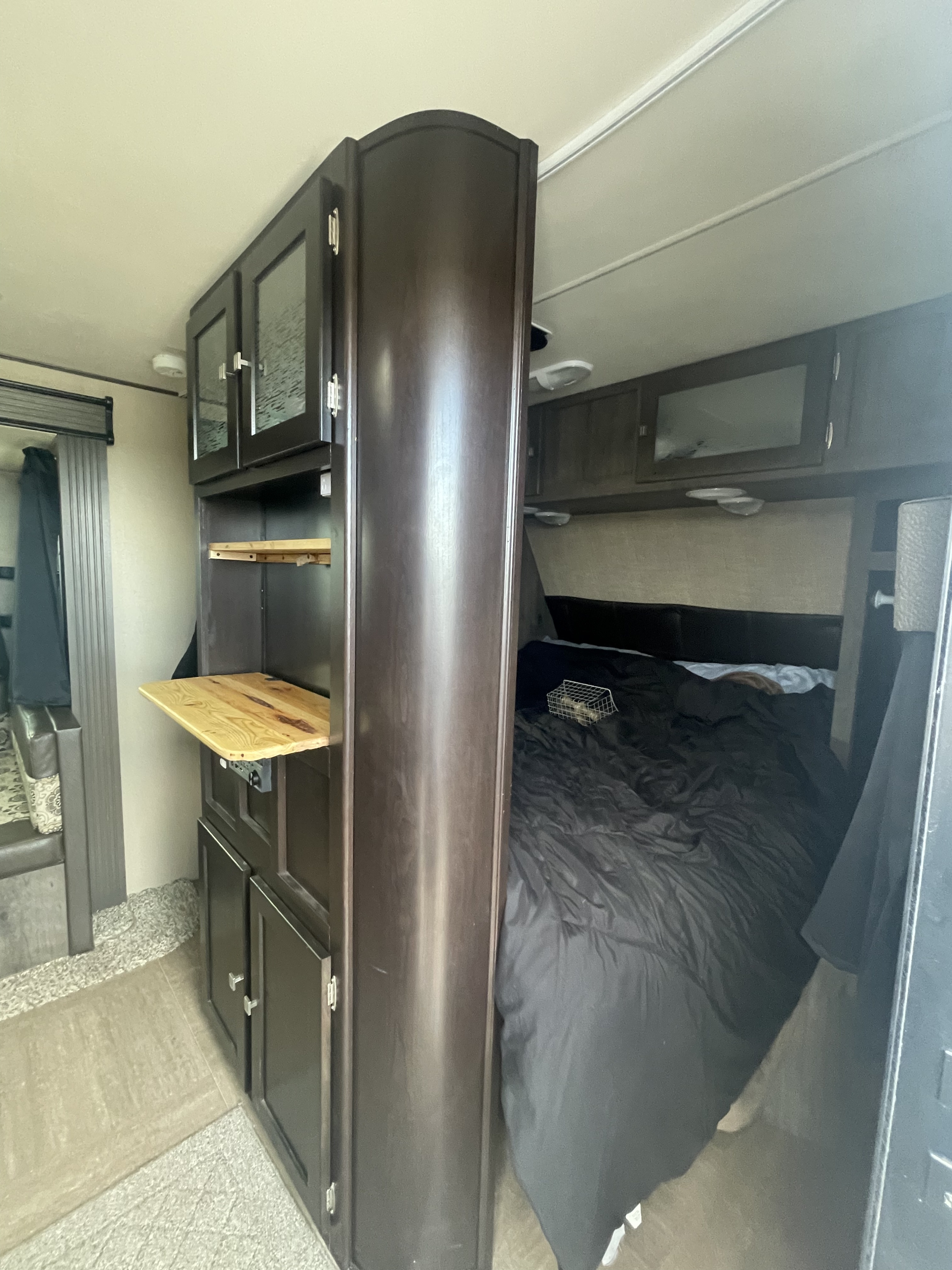 Explore this comfortable RV rental bedroom, featuring dark cabinetry, a spacious bed, and a handy fold-down shelf for convenience.. Dutchmen Kodiak 2016