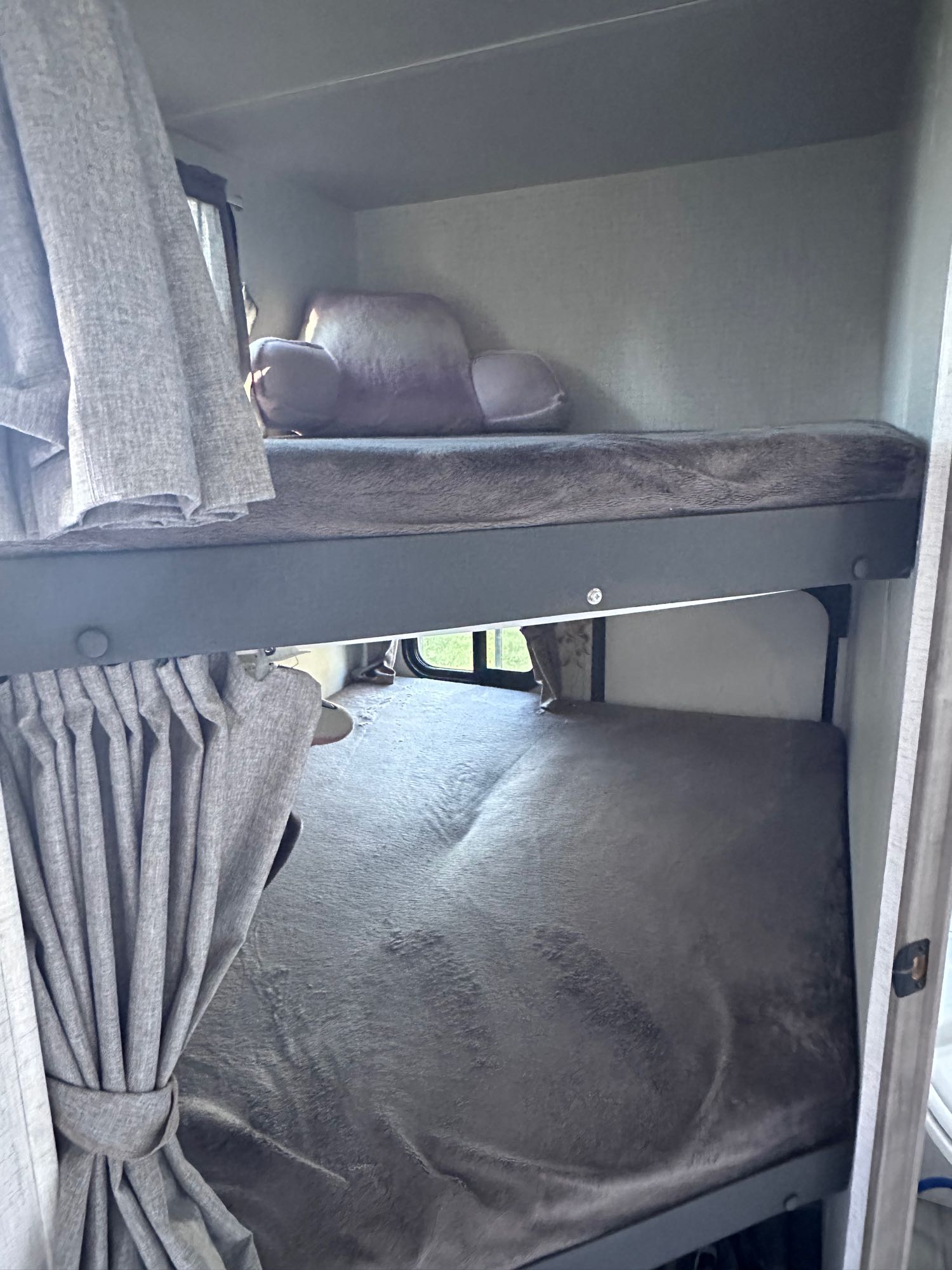 Compact RV rental with comfy grey bunk beds, featuring curtains and windows for a cozy mobile sleeping setup.. Winnebago Voyage 2022