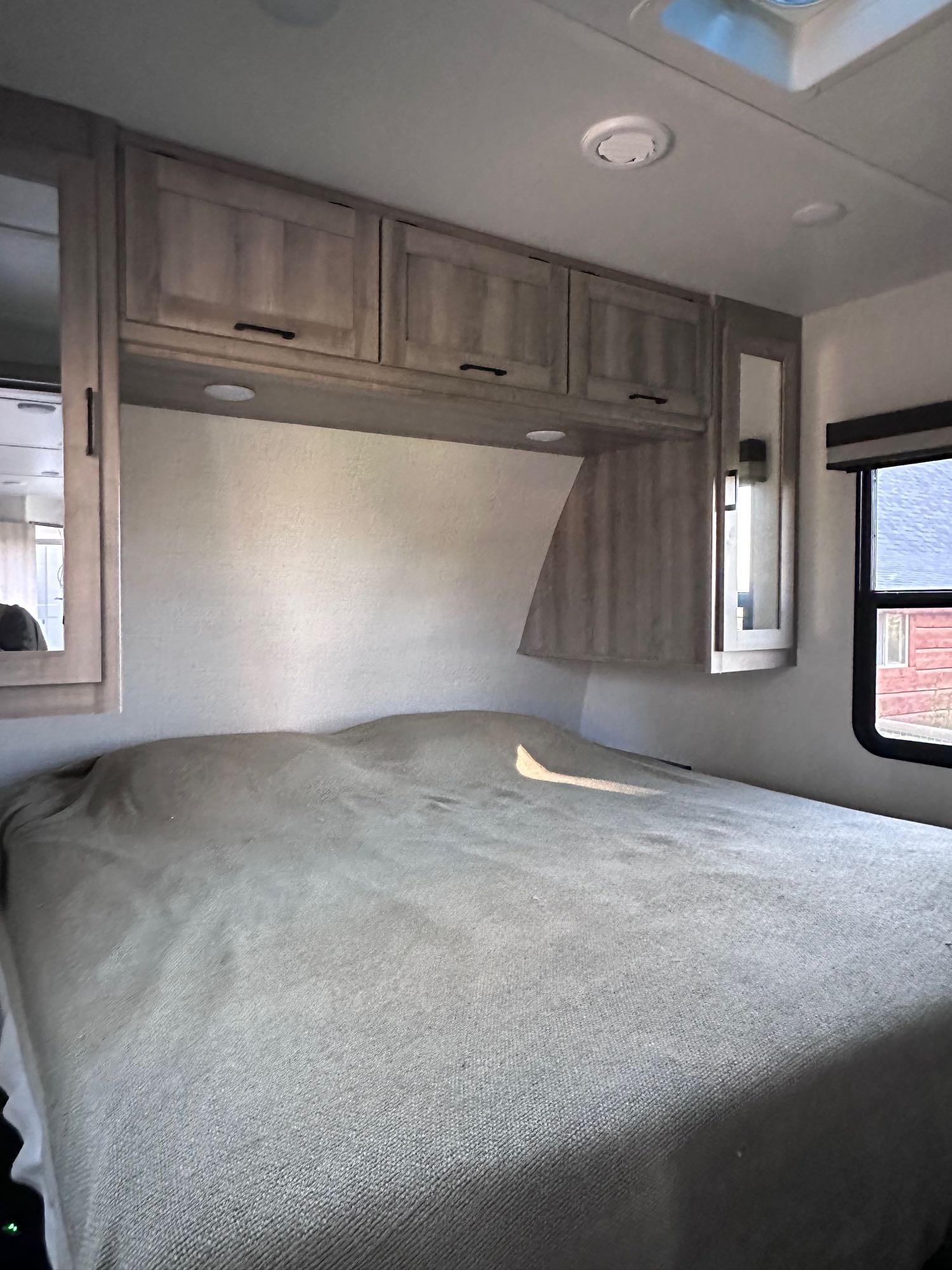 Explore this RV rental's cozy bedroom. Features a comfy bed, overhead cabinets, and built-in mirrors.. Winnebago Voyage 2022