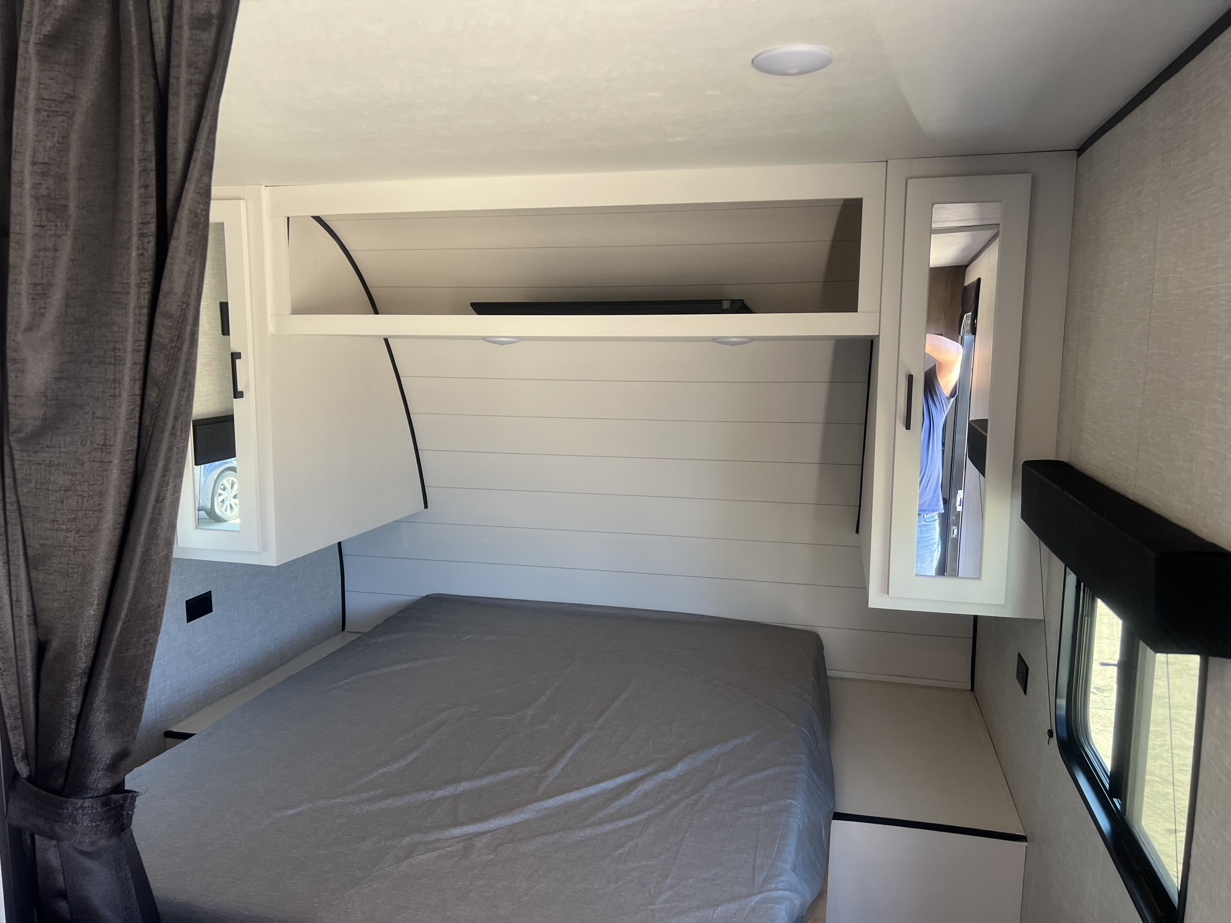 RV rental bedroom showcasing a bed, white overhead cabinets, shiplap walls, and a side window for a comfortable stay.. Jayco Jay Flight 2024