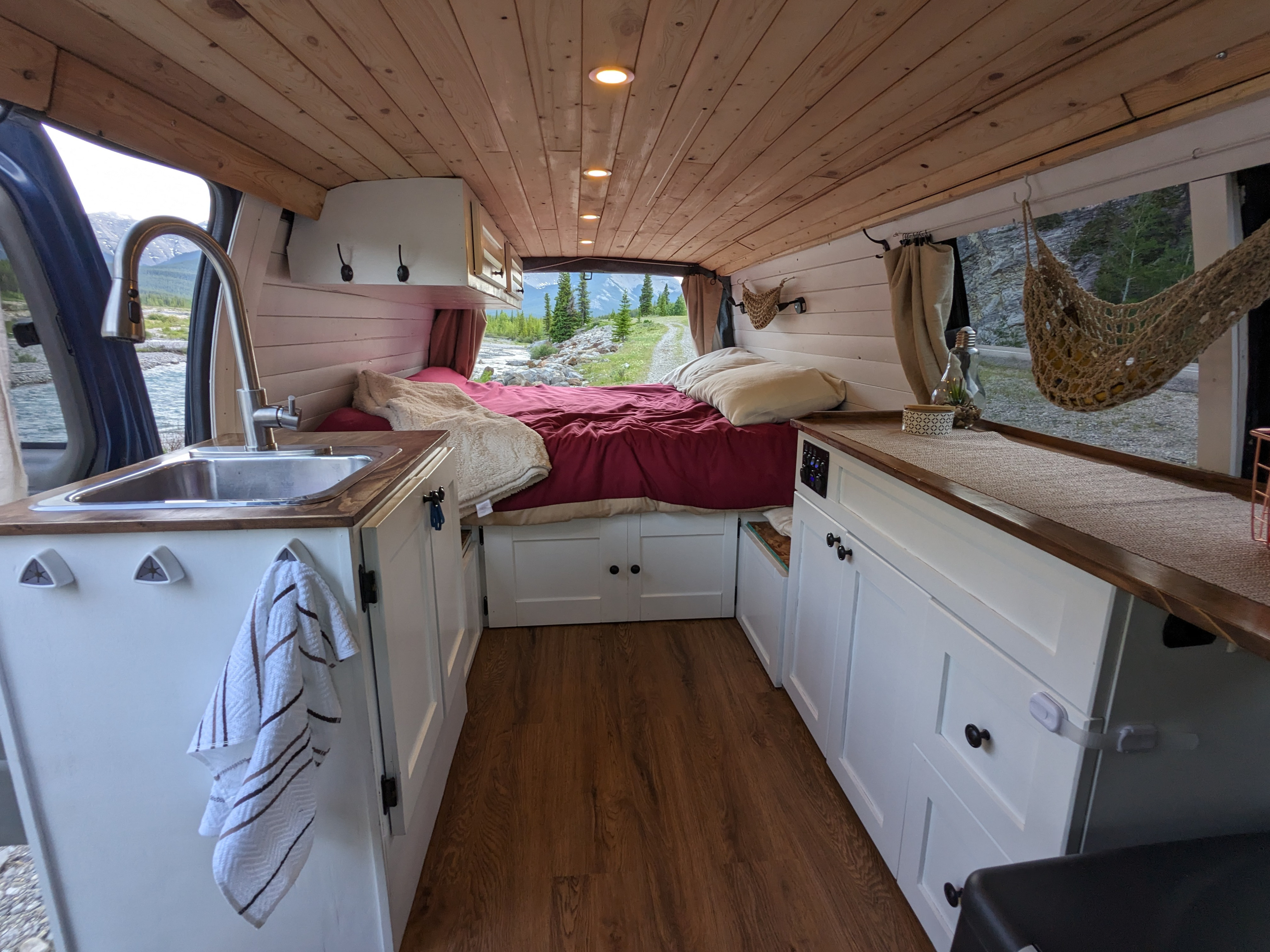 Cozy RV rental interior with a comfy bed, kitchen sink, and panoramic window views of mountains & a river.. Chevrolet Express 2003
