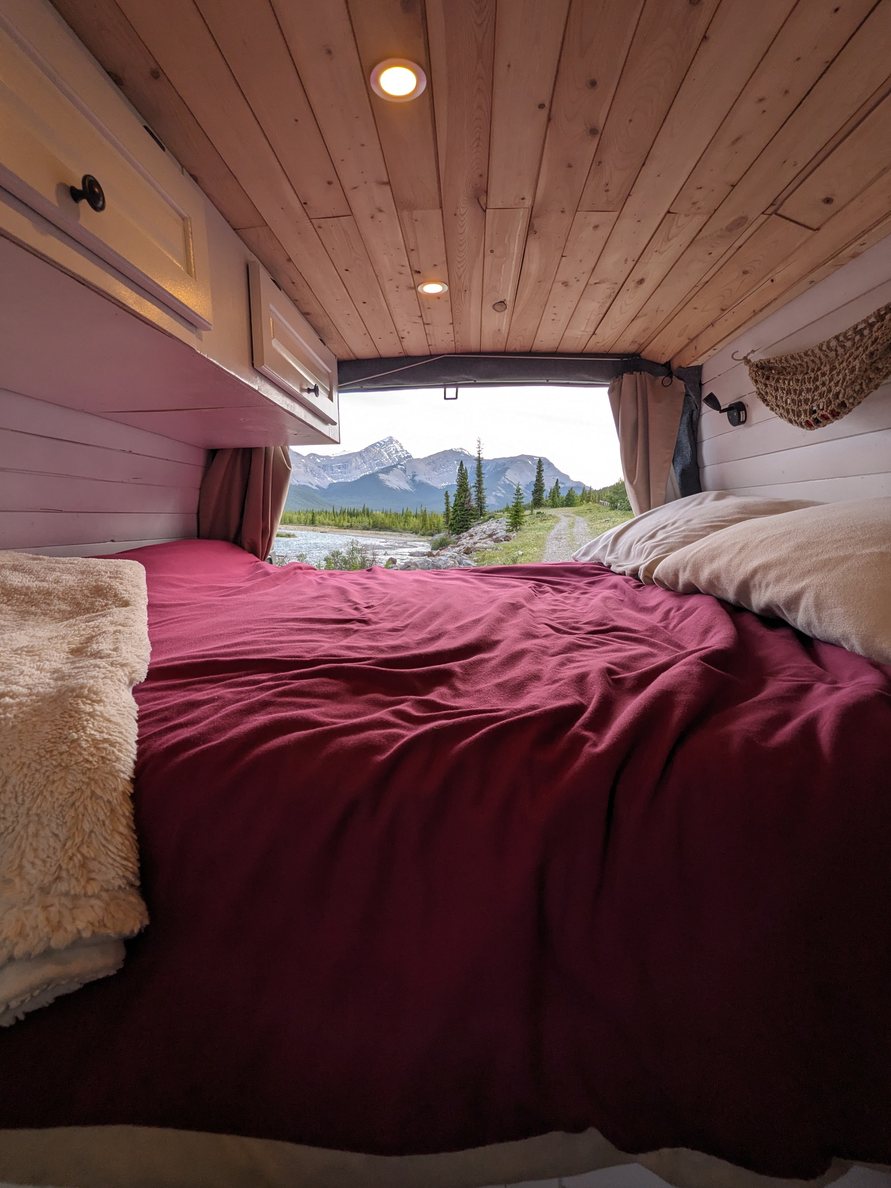 Cozy RV rental interior with a bed looking out to a mountain river view. Perfect for nature lovers.. Chevrolet Express 2003