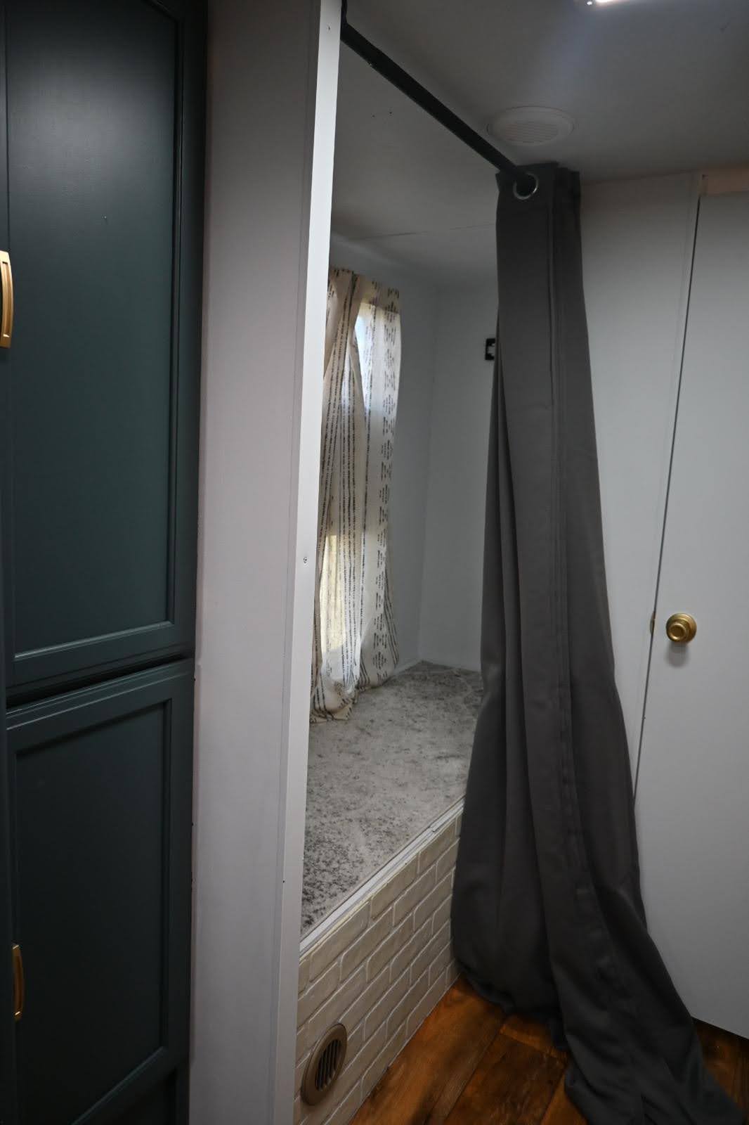 RV rental interior: A cozy, raised sleeping area with patterned rug, white brick trim, dark cabinets, and privacy curtain.. Keystone RV Passport Grand Touring 2015