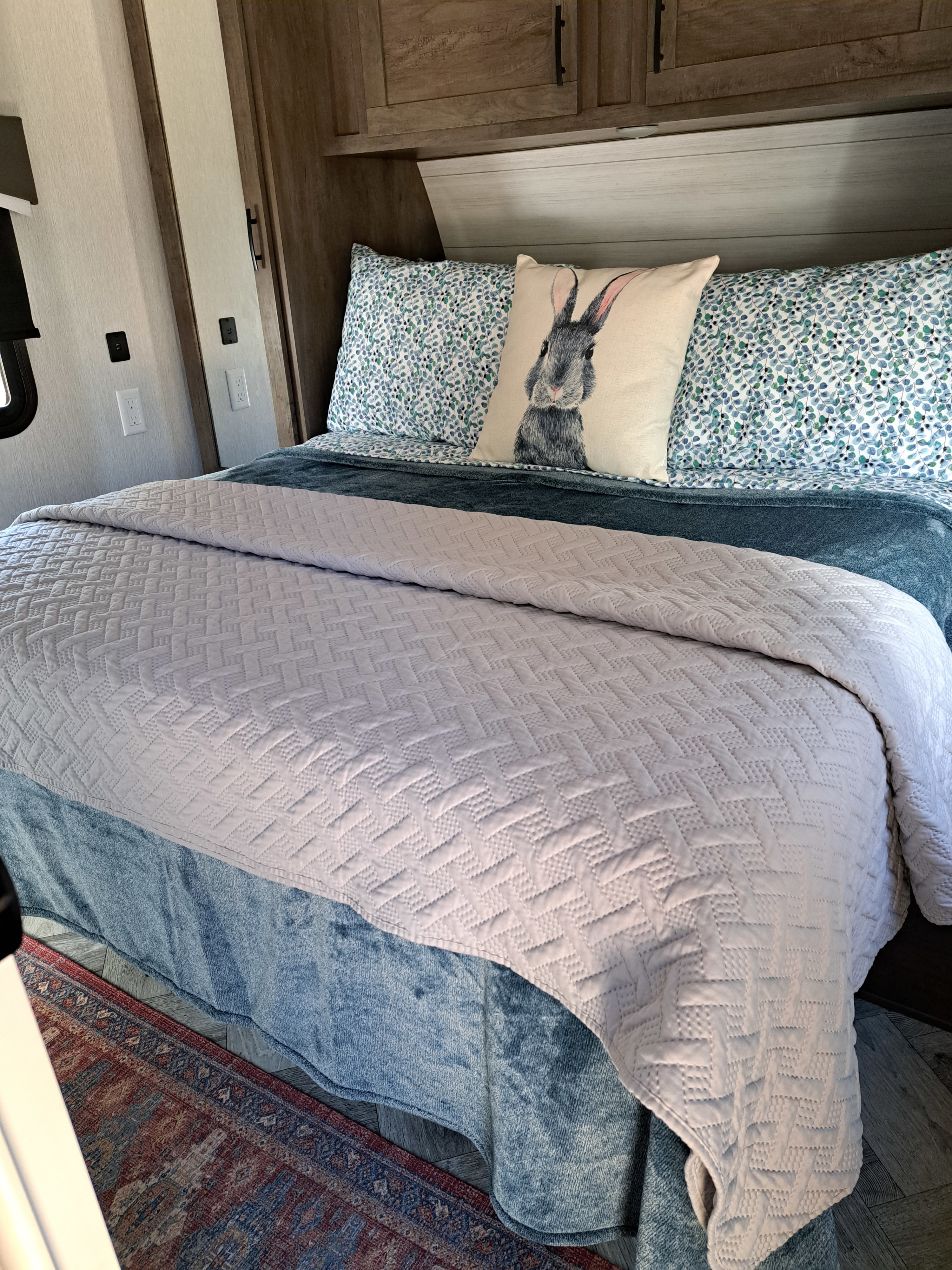 Serene RV rental bedroom featuring a comfy bed with a quilted comforter, blue patterned sheets, and a cute rabbit pillow.. Forest River Evo 2022