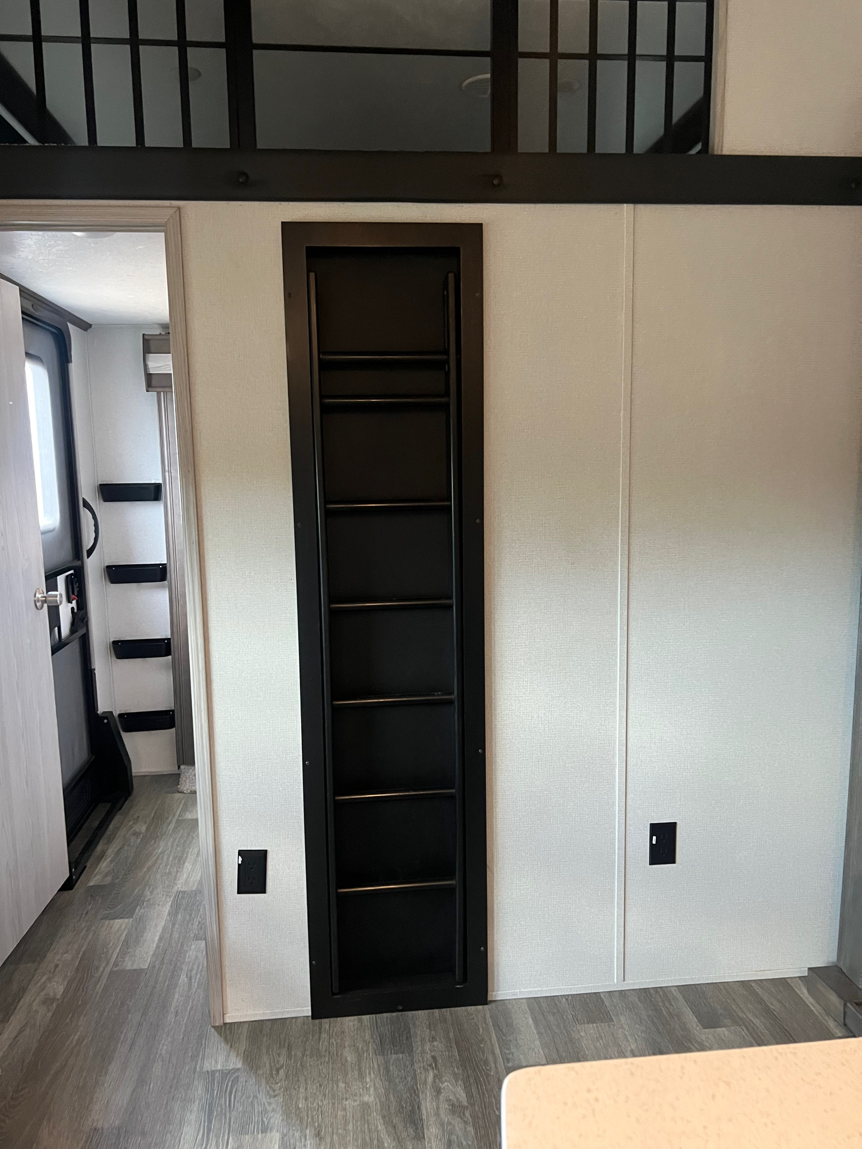 Inside this RV rental, a sleek black built-in ladder climbs to an upper sleeping loft, complemented by bright walls and a wood-patterned floor.. Keystone RV Montana High Country 2020