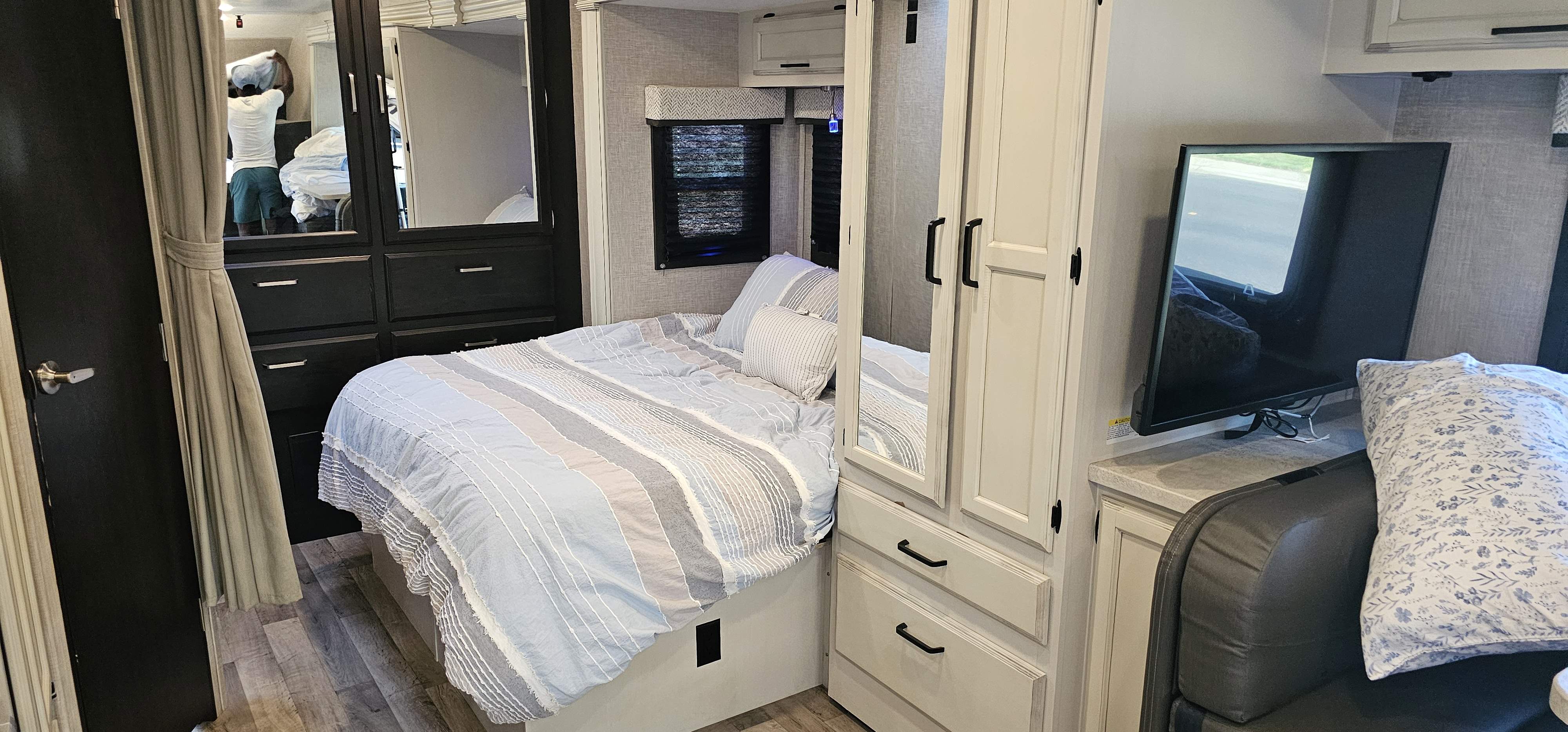 RV rental: inviting bedroom setup with striped bedding, mirrored closet, and TV. A person is reflected in the mirror.. Jayco Redhawk 2023