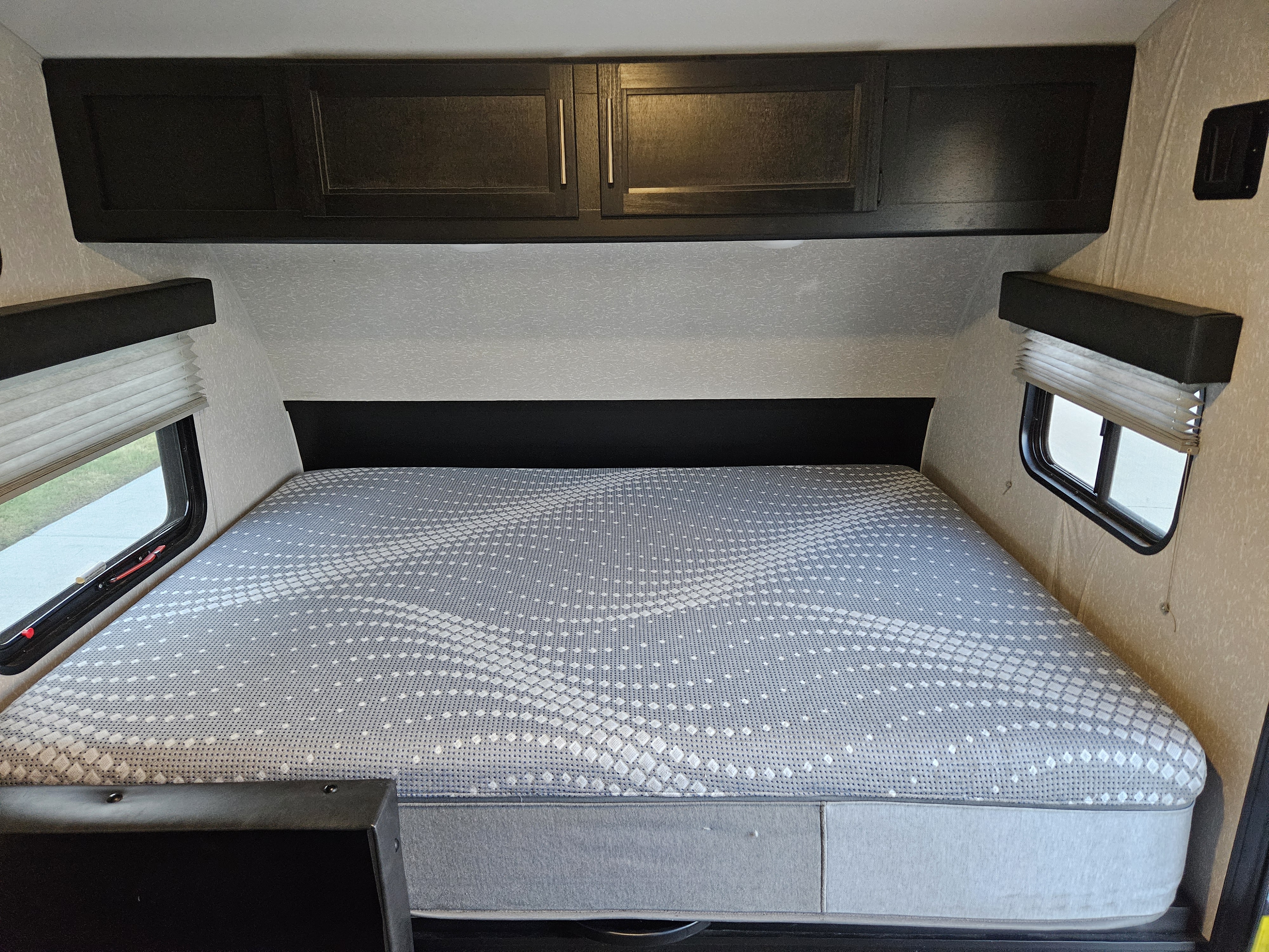Inside an RV rental, a patterned mattress on a bed, flanked by windows with blinds & overhead cabinets.. Forest River Cherokee Wolf Pup 2022
