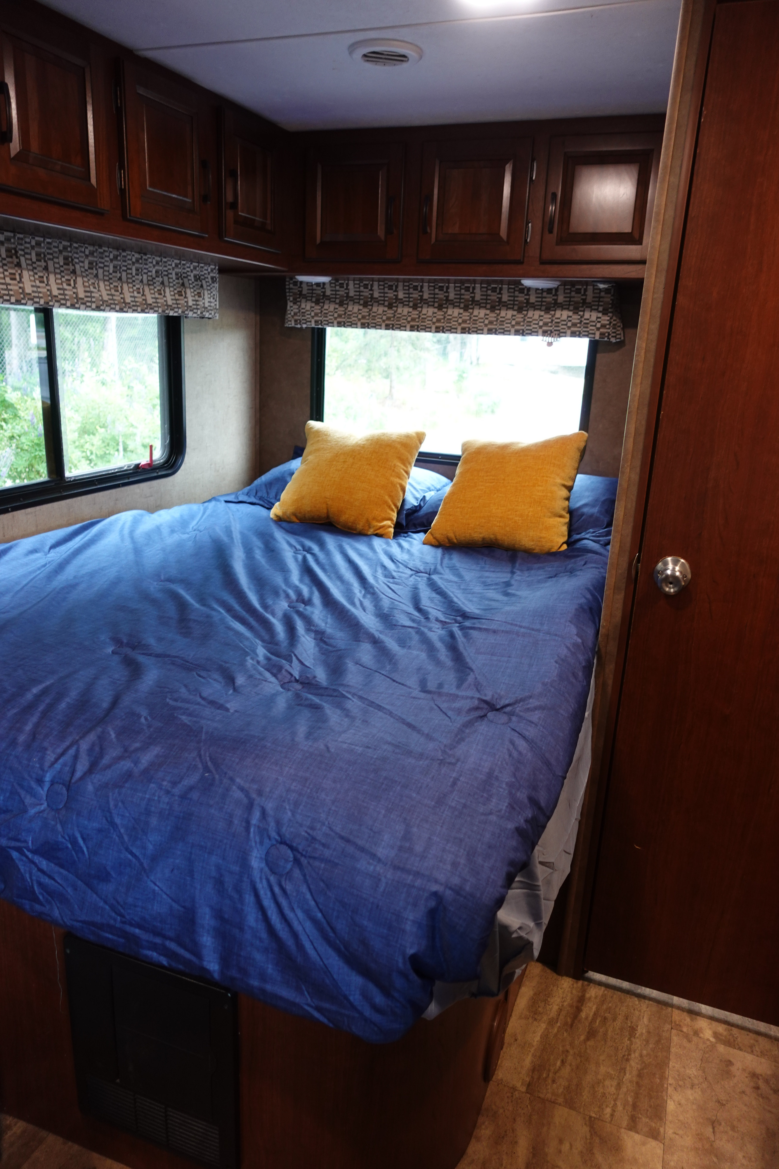 An inviting RV rental bedroom with a blue bed, yellow pillows, wood cabinets, and large windows.. Forest River Sunseeker 2017