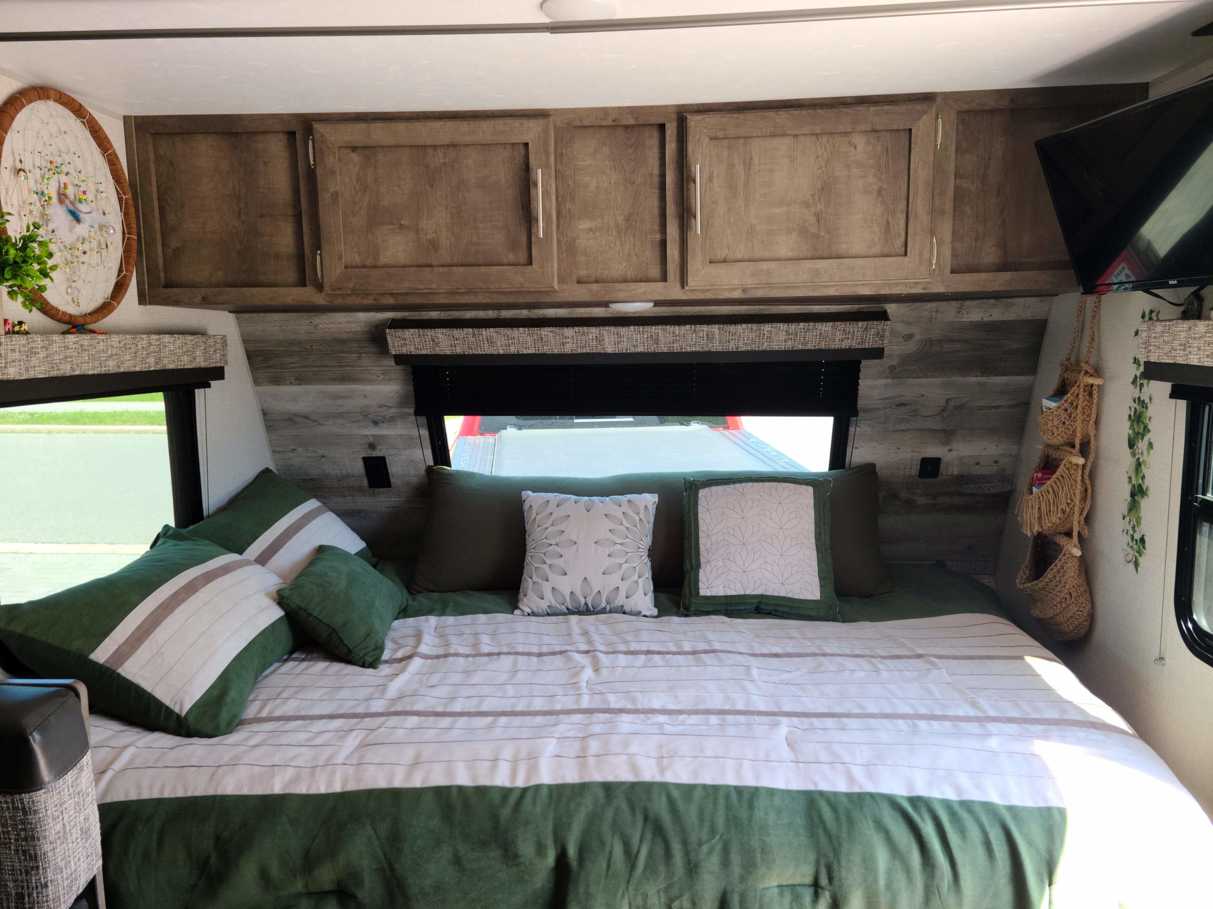 Cozy RV rental bedroom with comfortable bedding, overhead storage cabinets, and natural light from a window.. KZ Escape 2020