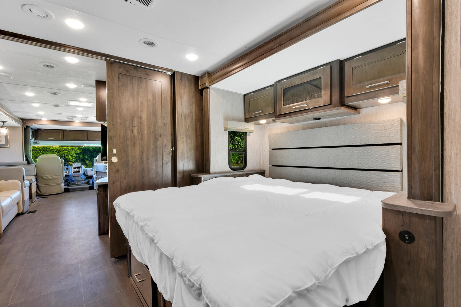 Spacious RV rental interior with a modern bedroom featuring a comfortable bed, overhead storage, and a view into the living area.. Coachman Mirada 2021