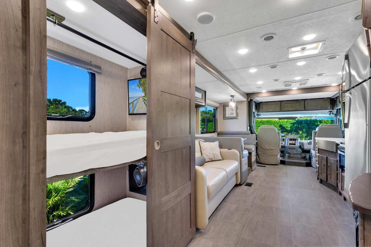 RV rental interior: bunk beds with outdoor views, sliding door to main living space with sofa, dining, kitchen, and cockpit.. Coachman Mirada 2021
