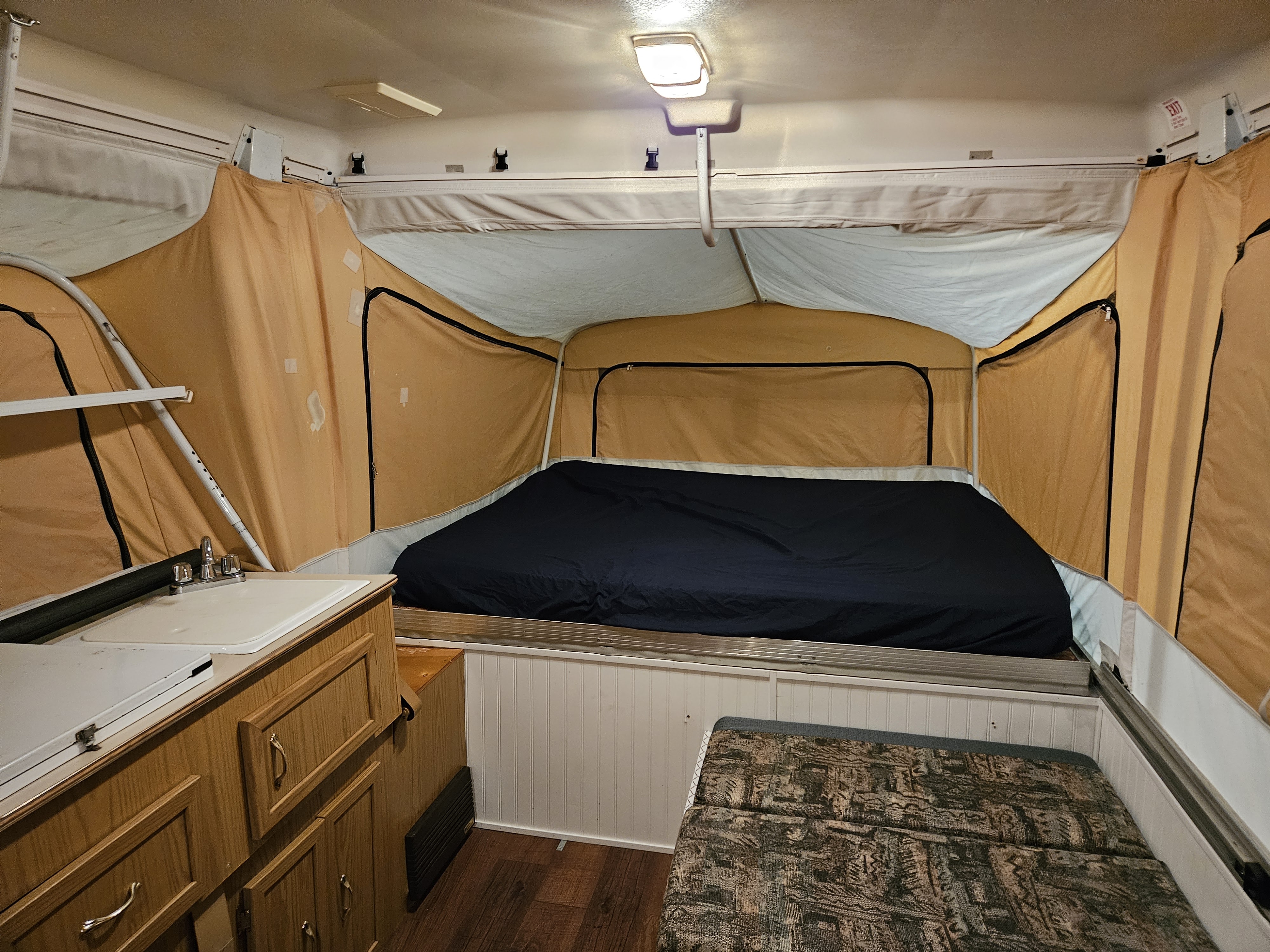 Cozy pop-up RV rental interior: large bed, sink, cabinets, and seating area for comfortable camping adventures.. Coleman Grand Tour Mesa 1999