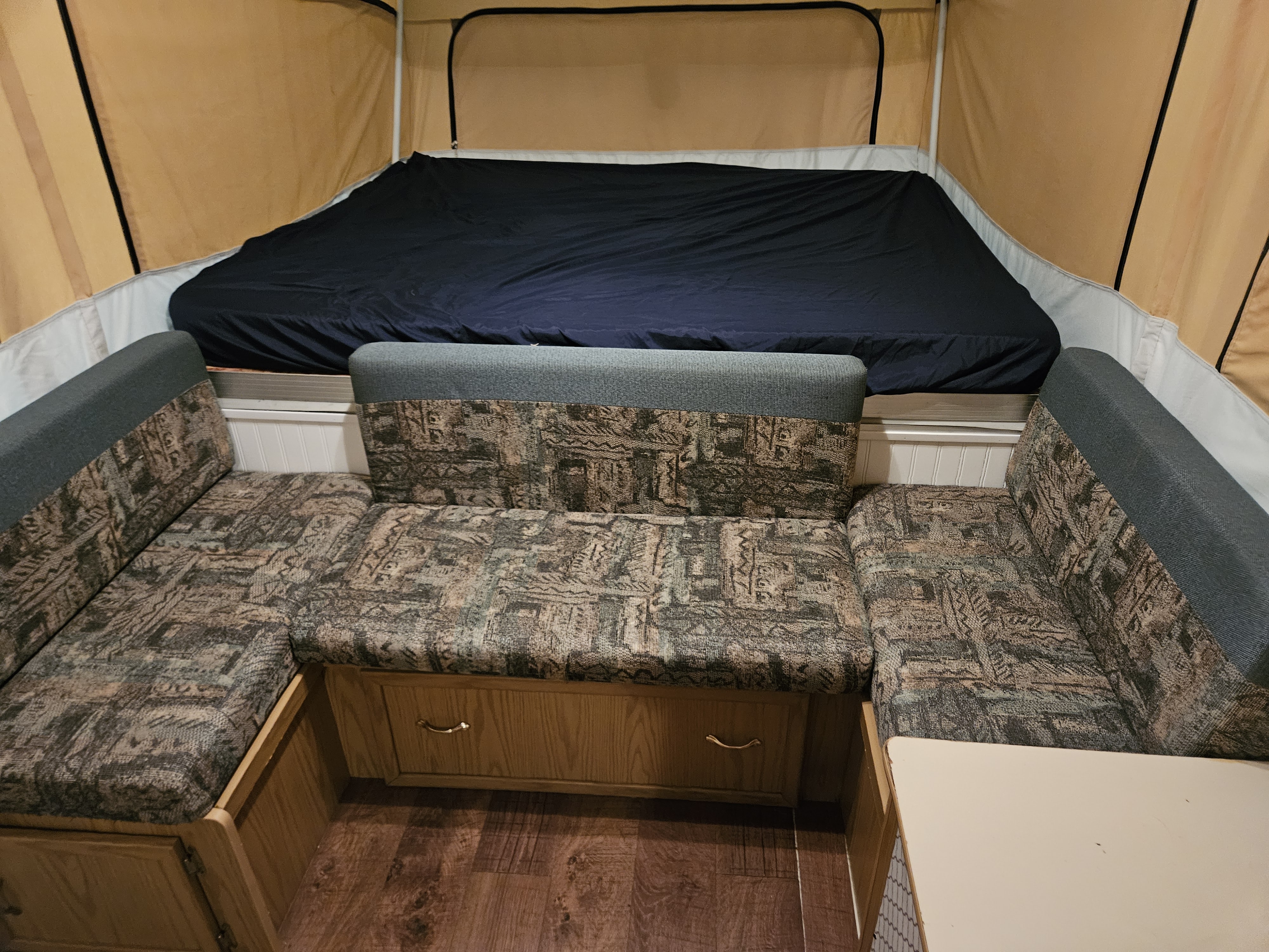 Pop-up camper RV rental interior: bed, U-shaped dinette with patterned cushions, and wood-look floor.. Coleman Grand Tour Mesa 1999