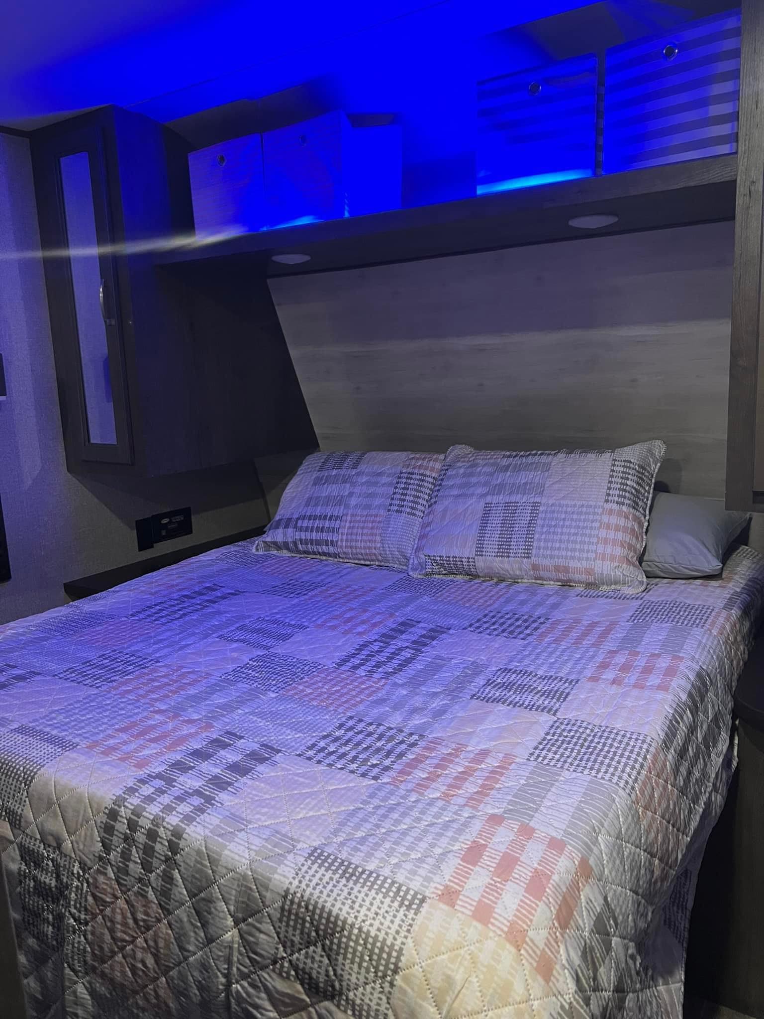 Inside an RV rental: a cozy bedroom featuring a patterned bed, overhead storage, and ambient blue LED lighting.. Jayco Jay Flight SLX 2022
