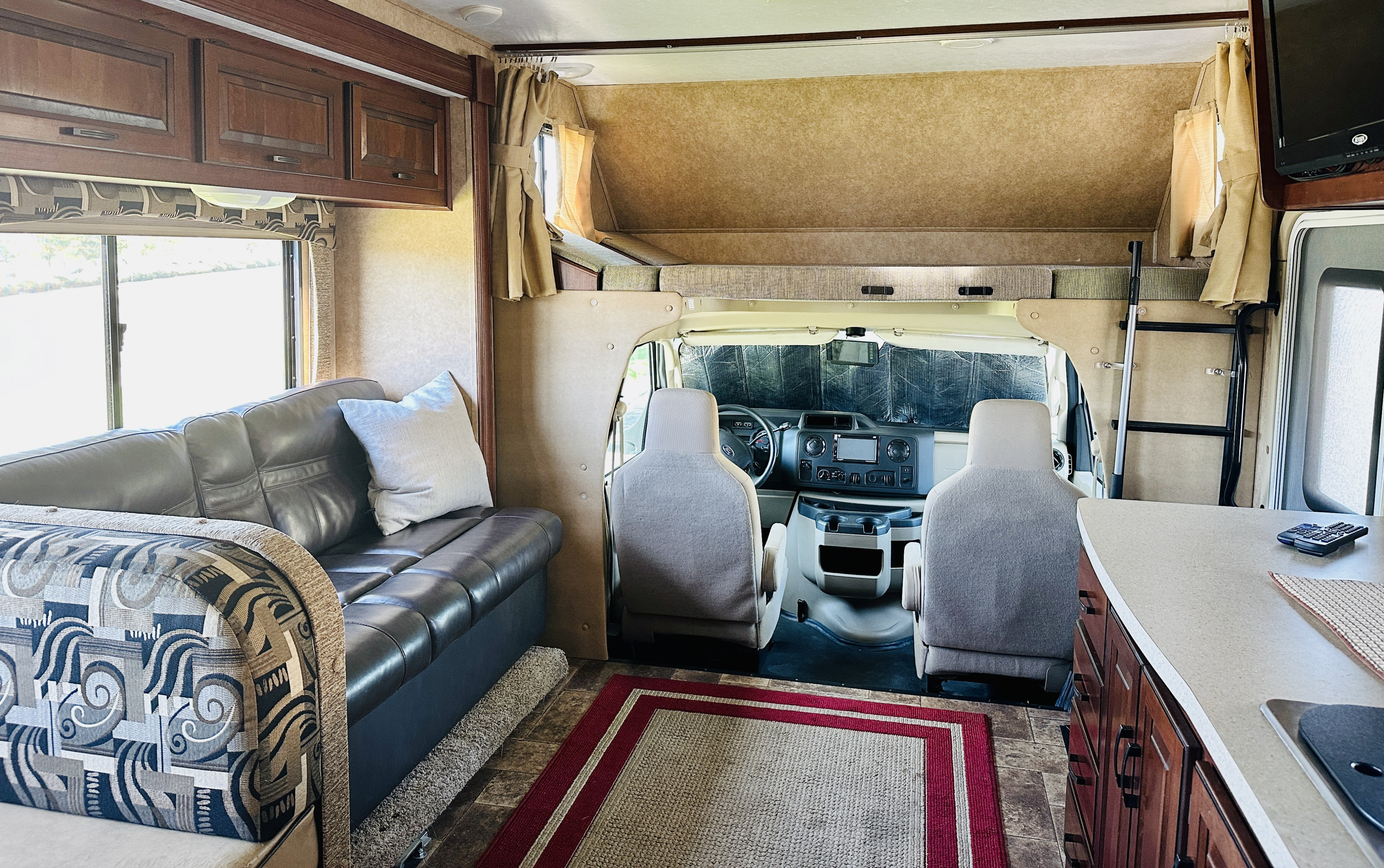 Spacious RV rental interior featuring a cozy living area, kitchen, cockpit, and an overhead bunk bed for comfortable travel.. Forest River Sunseeker 2014