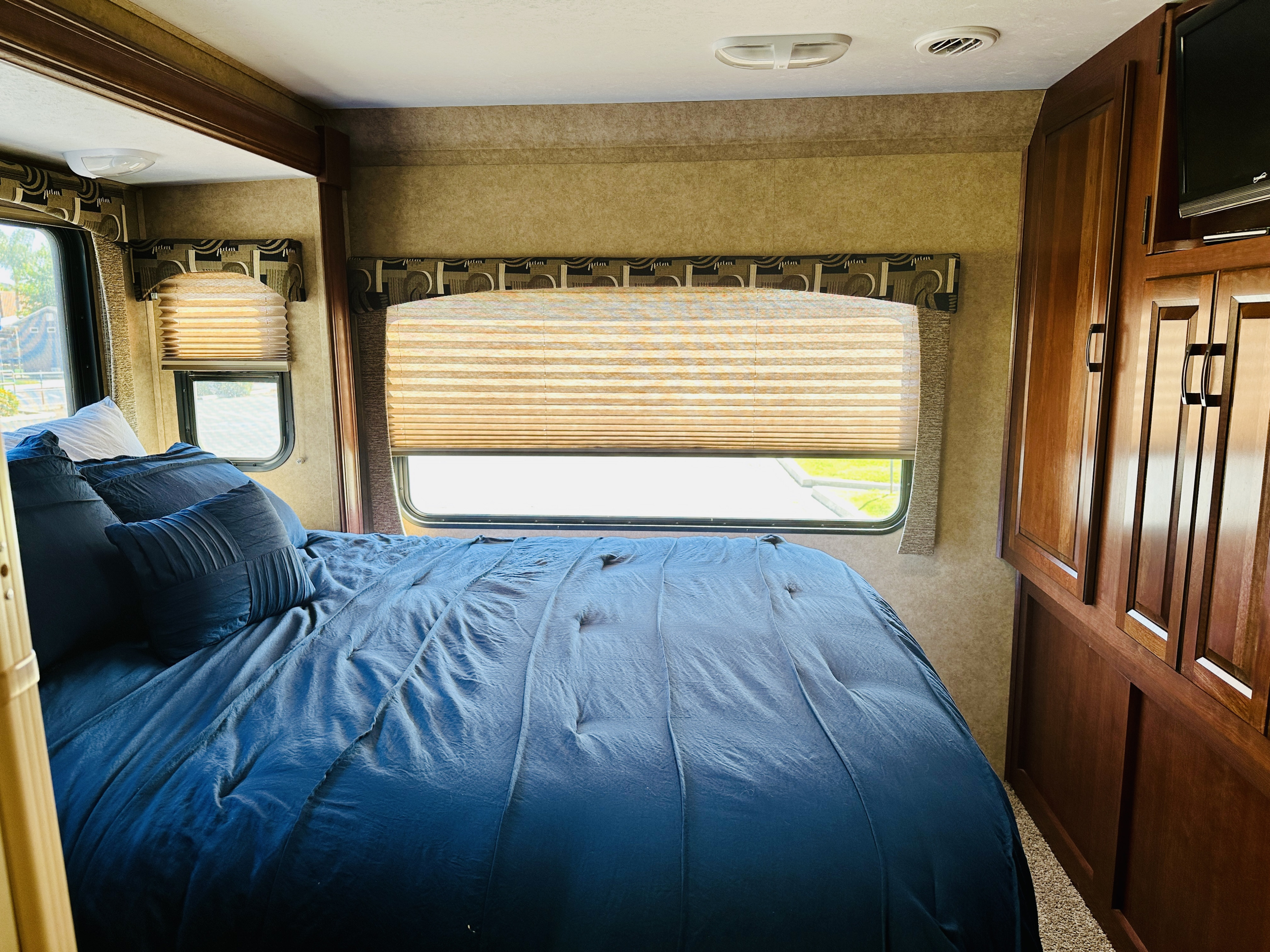 Enjoy comfortable sleeping in this RV rental bedroom, featuring a blue bed, windows with blinds, and wooden cabinets.. Forest River Sunseeker 2014
