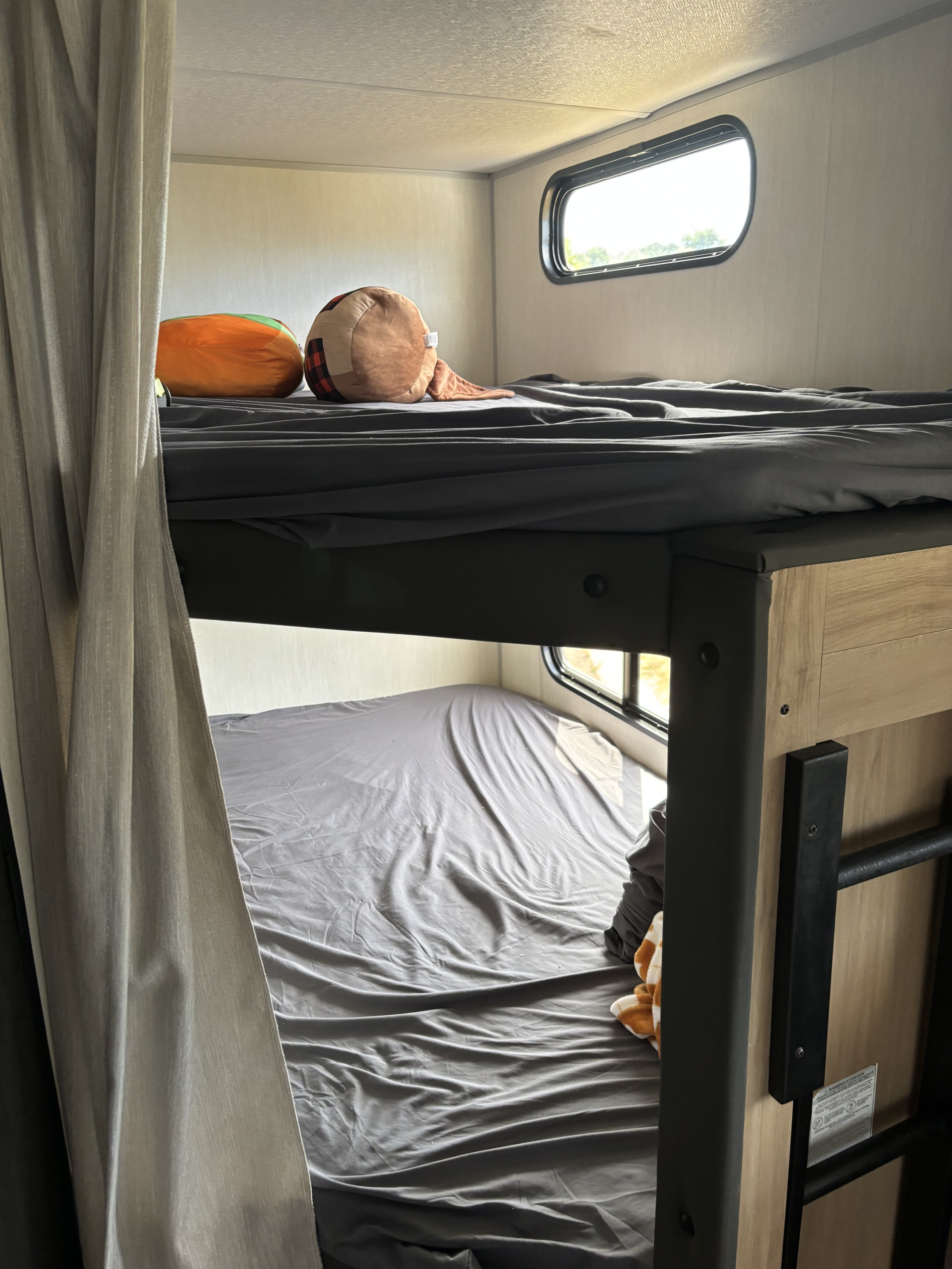 Inside an RV rental: comfortable bunk beds with gray bedding, pillows, and small windows, perfect for travel.. Forest River Cherokee 26DBH 2024