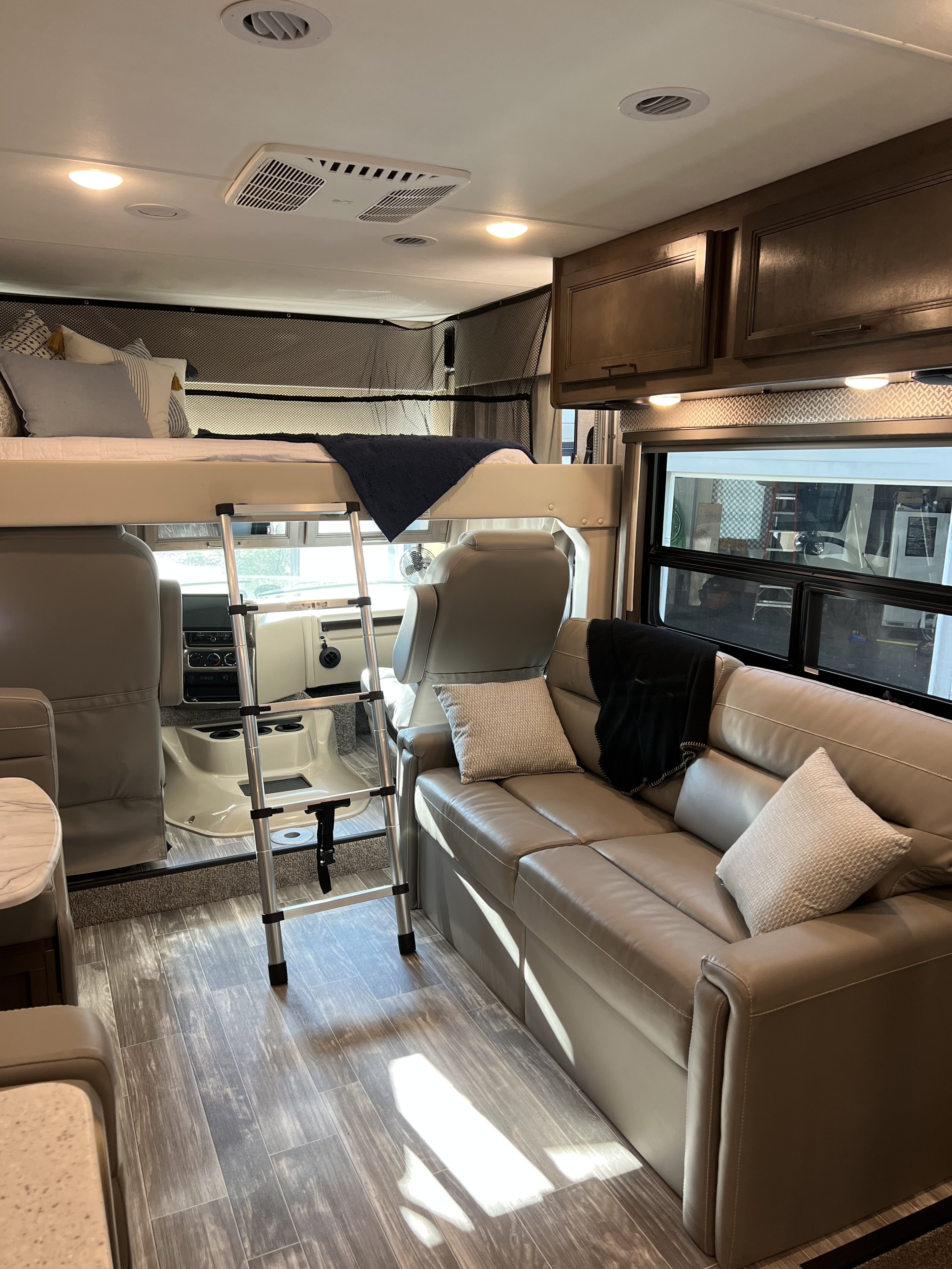 RV rental living area featuring a cozy sofa, overhead bunk bed with ladder, and wood-look flooring.. Thor Hurricane 2022