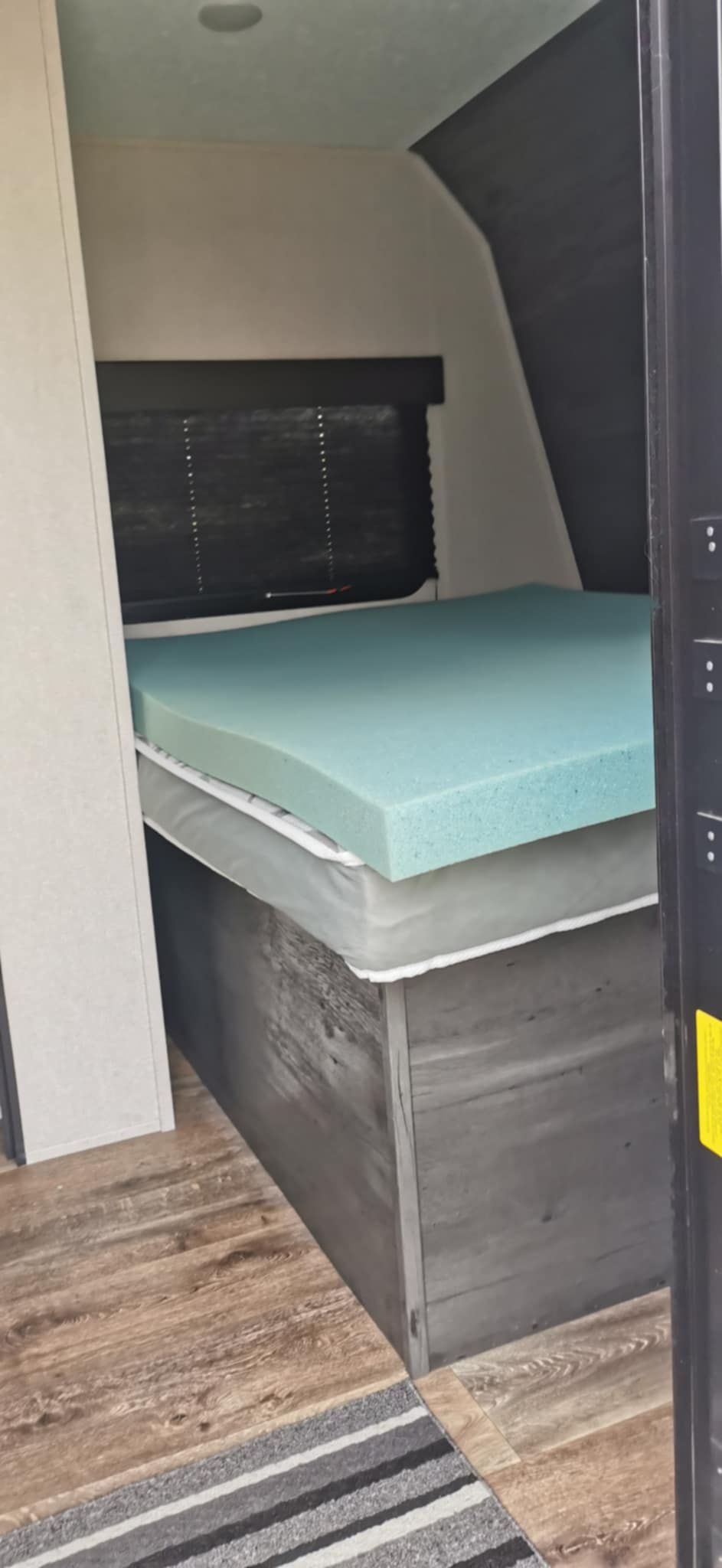 RV rental sleeping space: Bed with a soft blue foam topper, wood-look floor, and window blind.. Keystone RV Hideout 2020