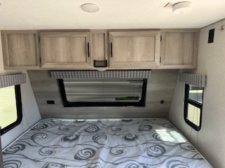 Inside this RV rental, find a comfortable bedroom: a bed with patterned mattress, overhead cabinets, and multiple windows.. Sportsmen 181BH 2022