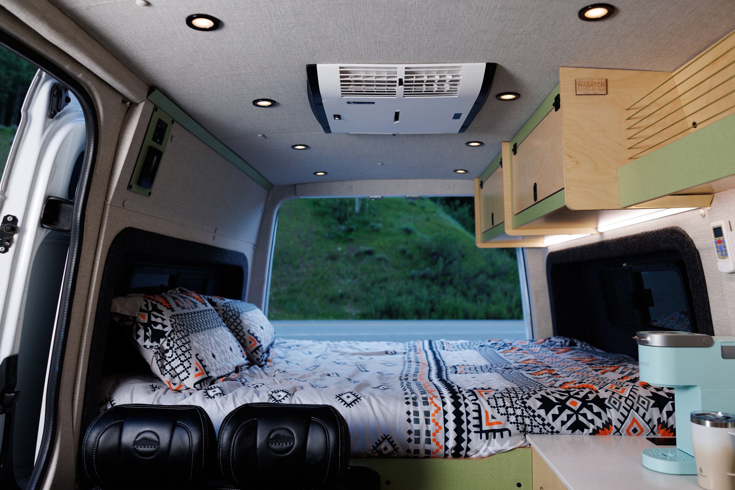 Inside this cozy rv rental: a bed with geometric bedding, AC unit, custom storage, and coffee station, with nature views.. Mercedes Sprinter 2017