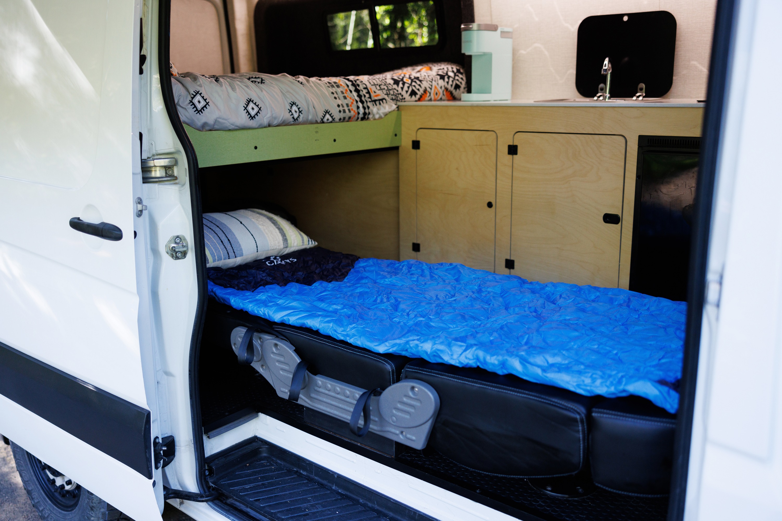 Inside an rv rental camper van, a view through the open door shows bunk beds with sleeping bags and a compact kitchen.. Mercedes Sprinter 2017