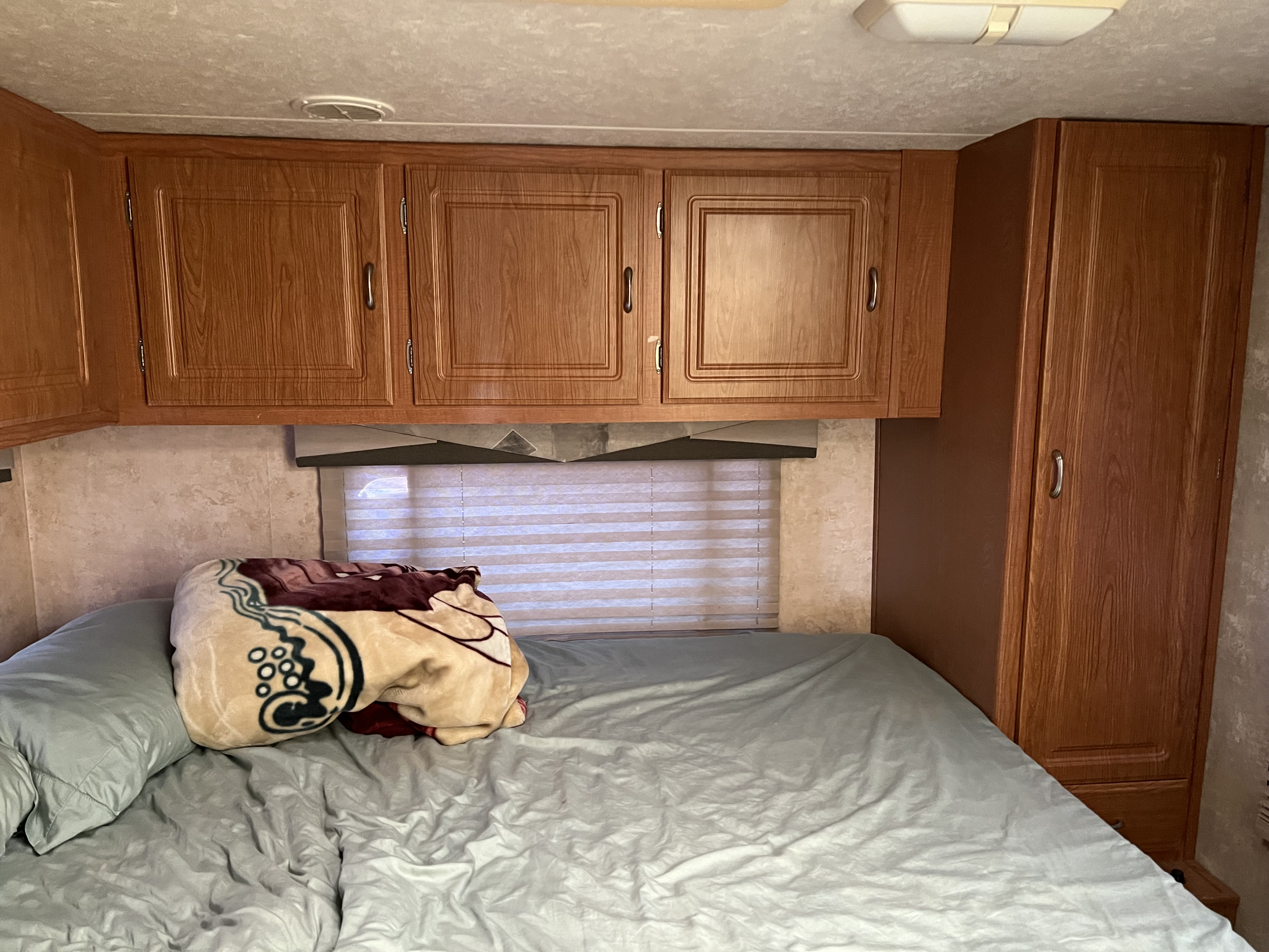 Cozy RV rental bedroom featuring a neatly made bed, overhead wooden cabinets, and a tall wardrobe with a window view.. Coachmen Freelander 2007